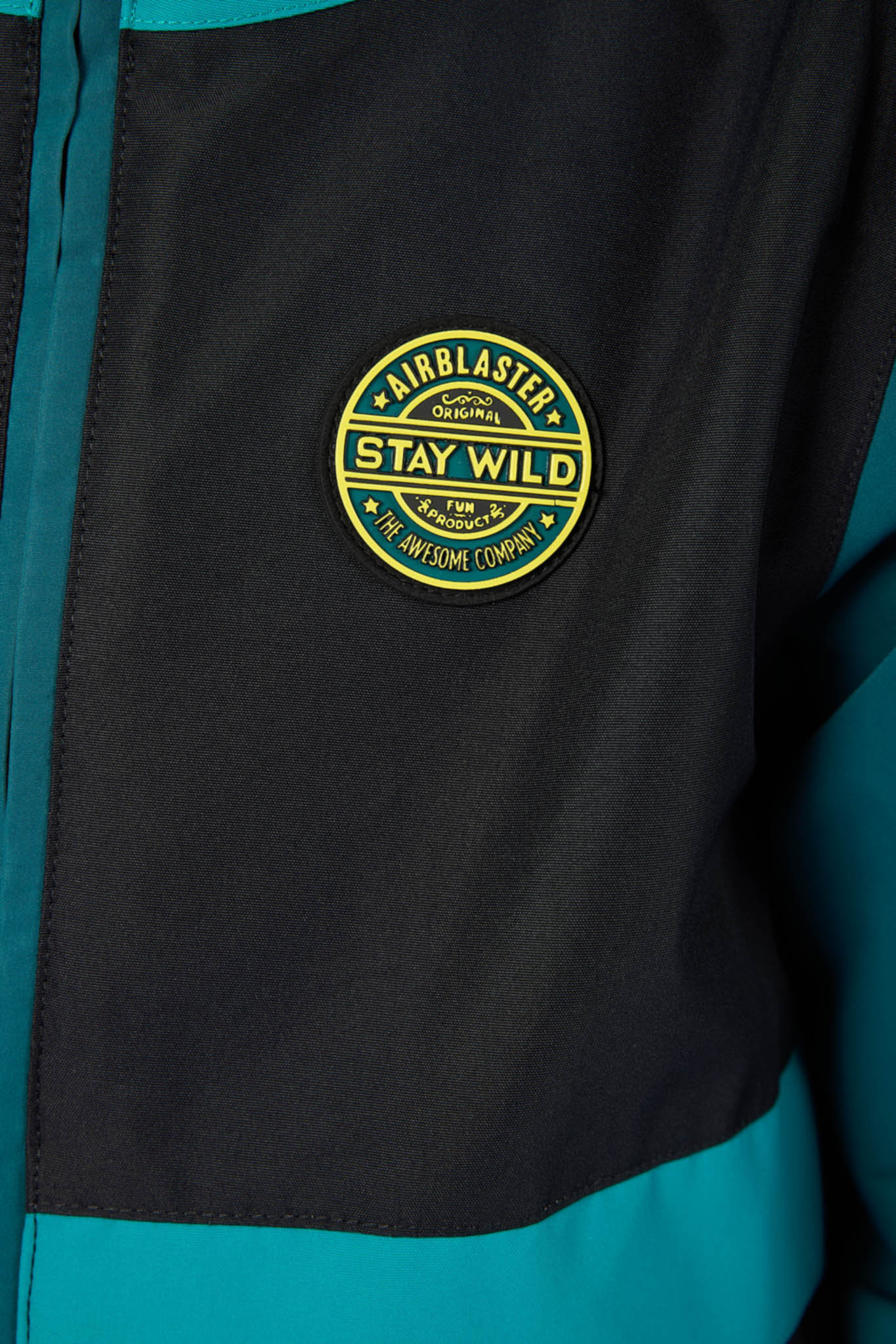 Close-up of a black and teal jacket featuring a circular yellow and green 'Airblast' logo patch on the chest.