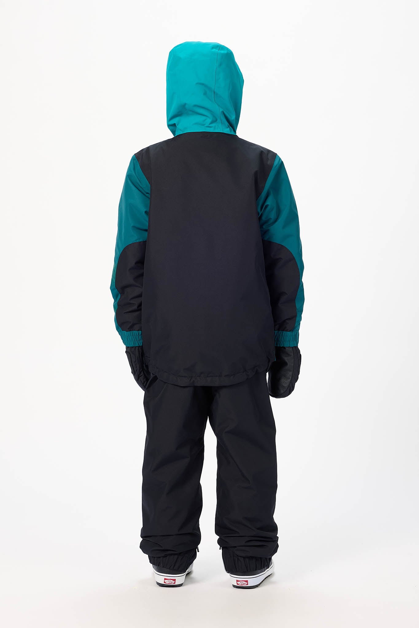 A child viewed from the back wearing a colorblock snowboard jacket with a black body, teal hood and sleeves, black pants, and black gloves, set against a plain white studio background.
