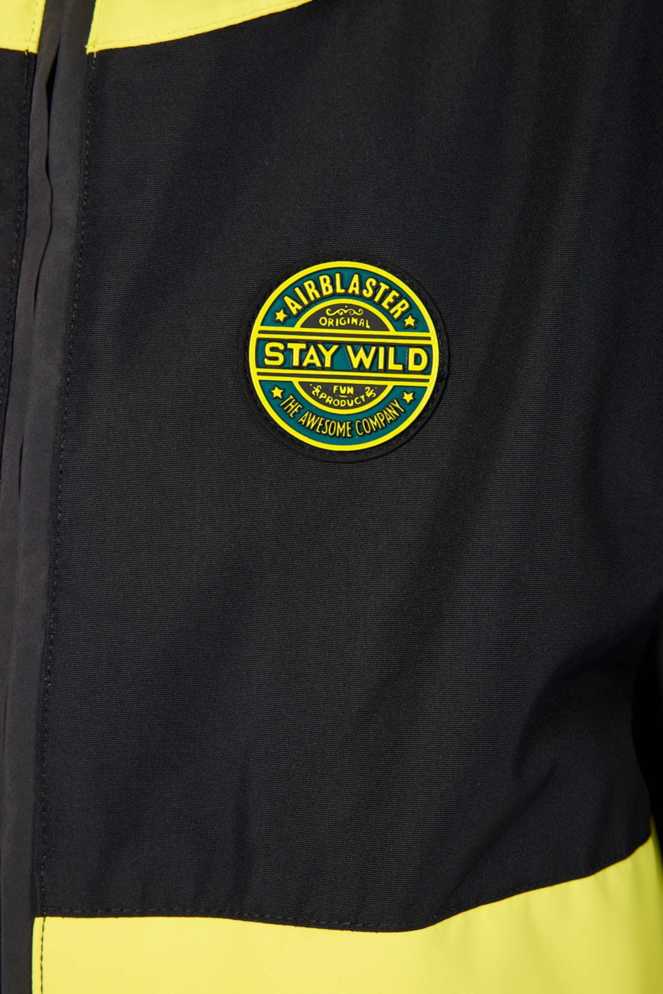 Close-up of a black jacket with bright yellow contrast panels and a circular yellow and green embroidered patch reading 'Airblaster Stay Wild' on the chest.