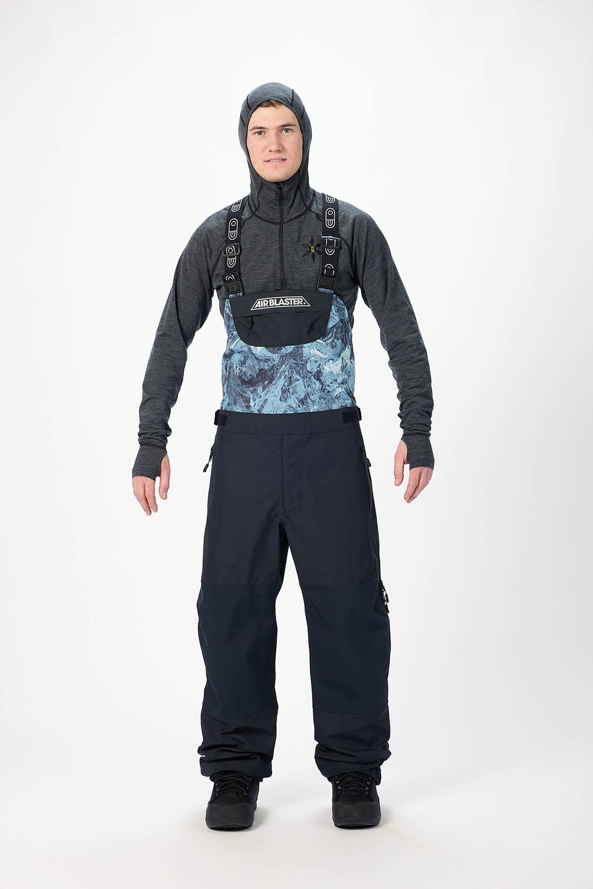 Person wearing a black hooded jacket and black pants with a blue patterned chest area on a white background