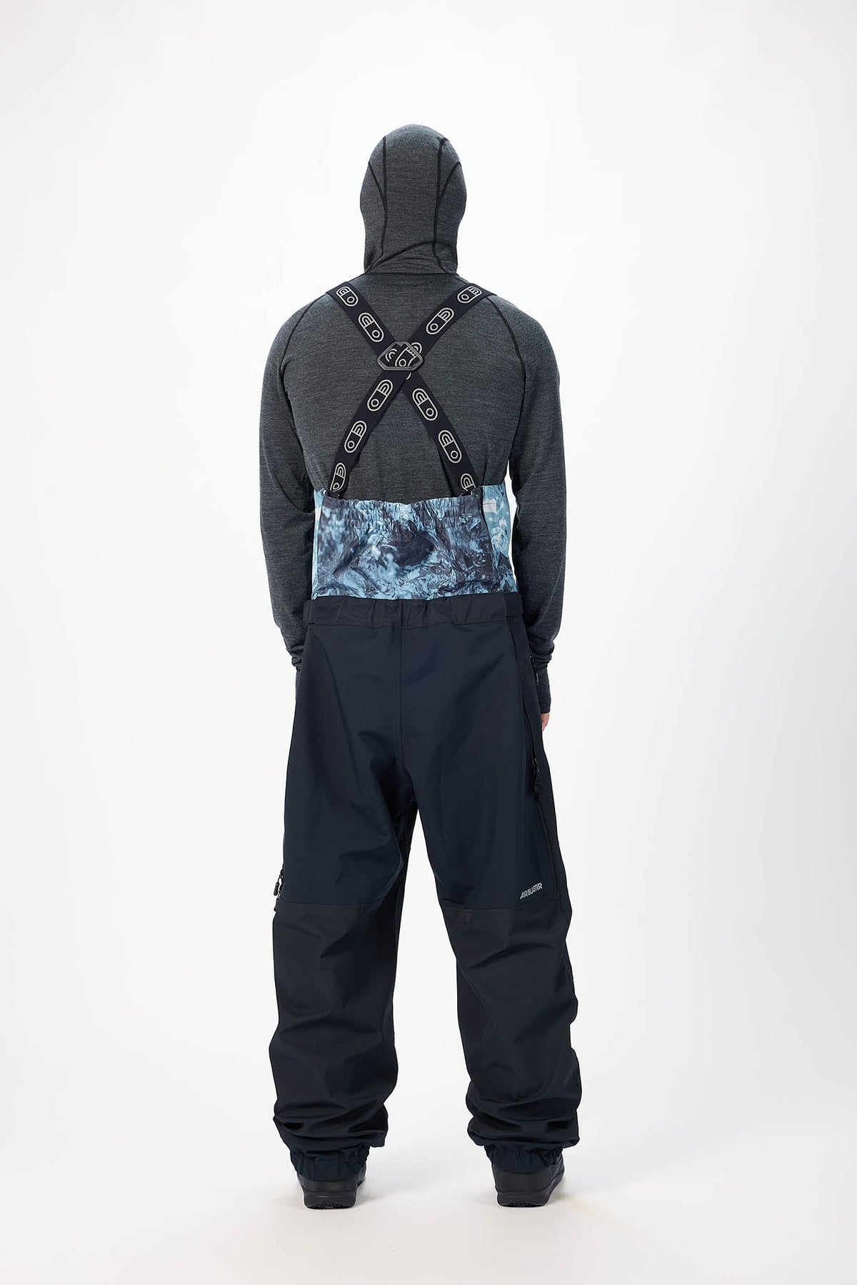 Person wearing a black snowsuit with blue patterned back panel on a white background