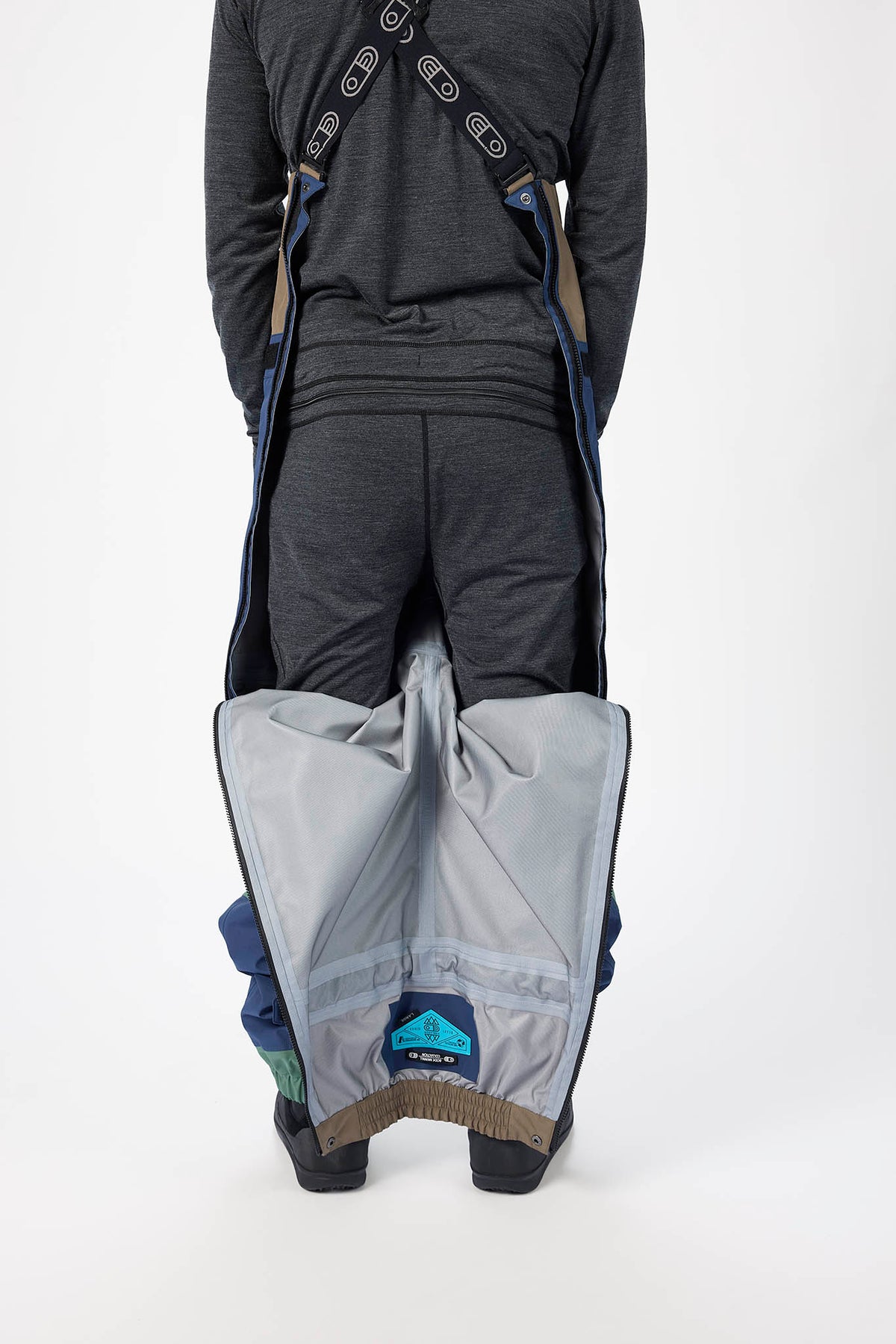 Person wearing a gray jacket and black pants with a gray sleeping bag on a white background