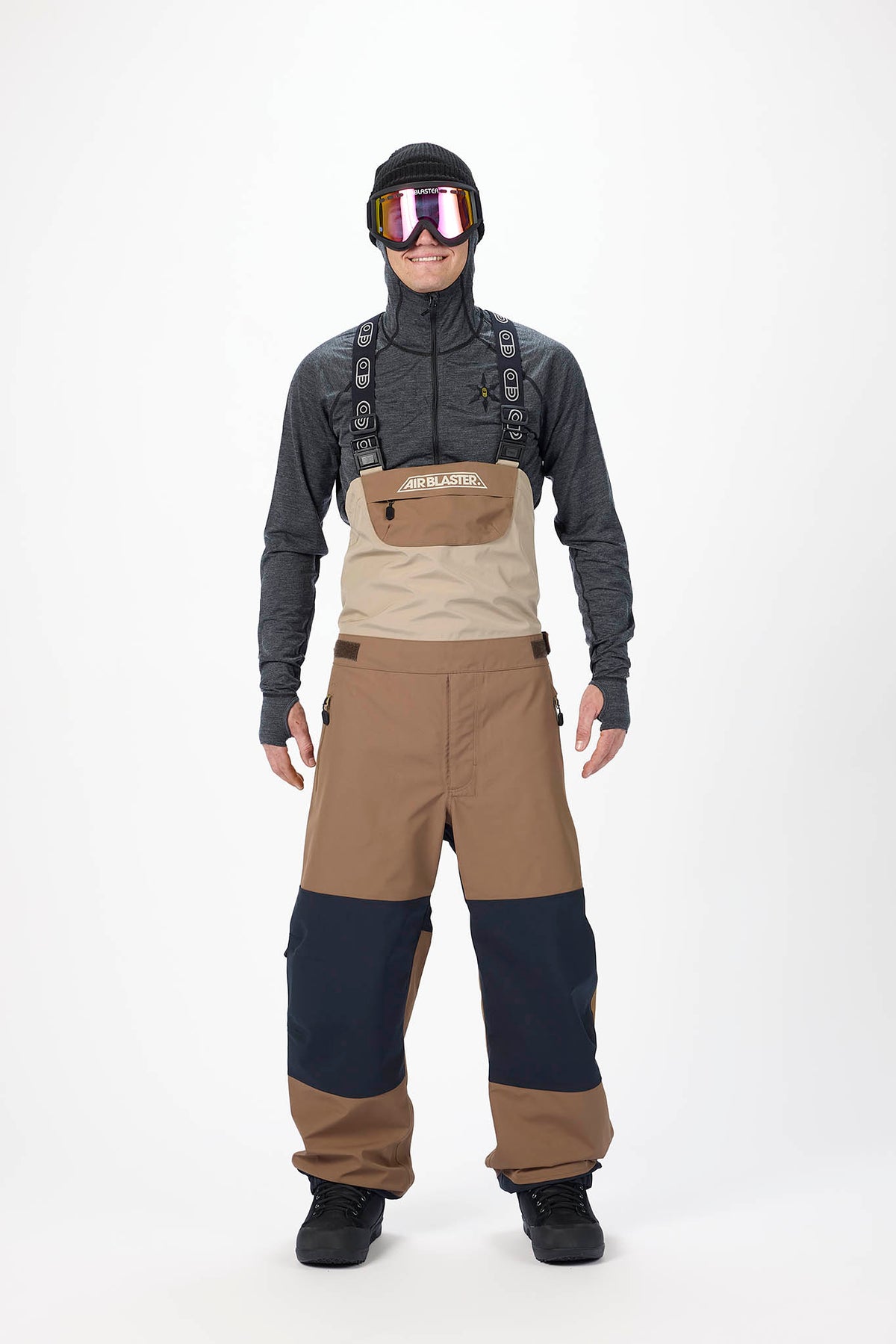 Person wearing a gray long-sleeve shirt, beige bib overalls, and black boots on a white background