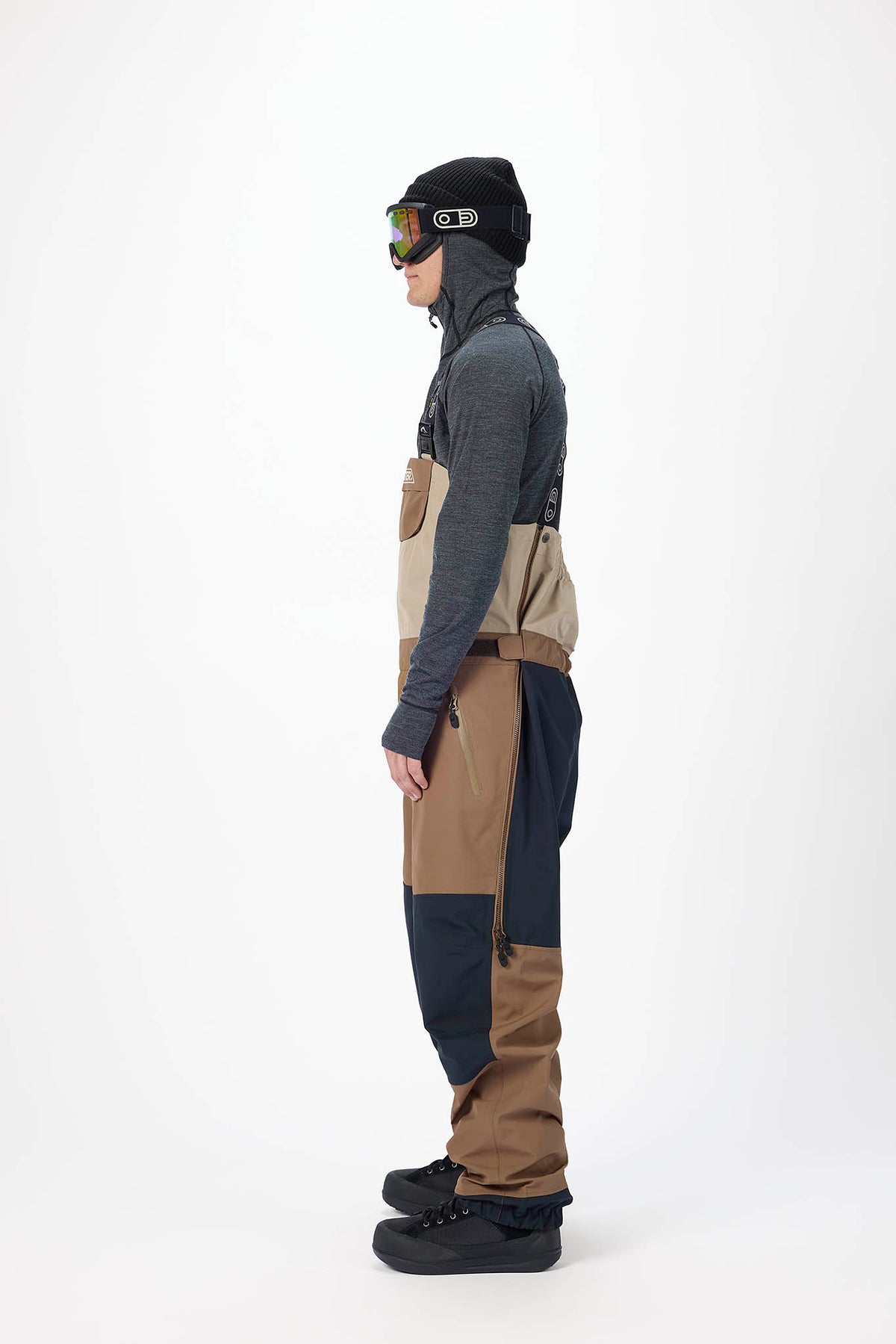 Person wearing a gray jacket, black beanie, and brown pants on a white background