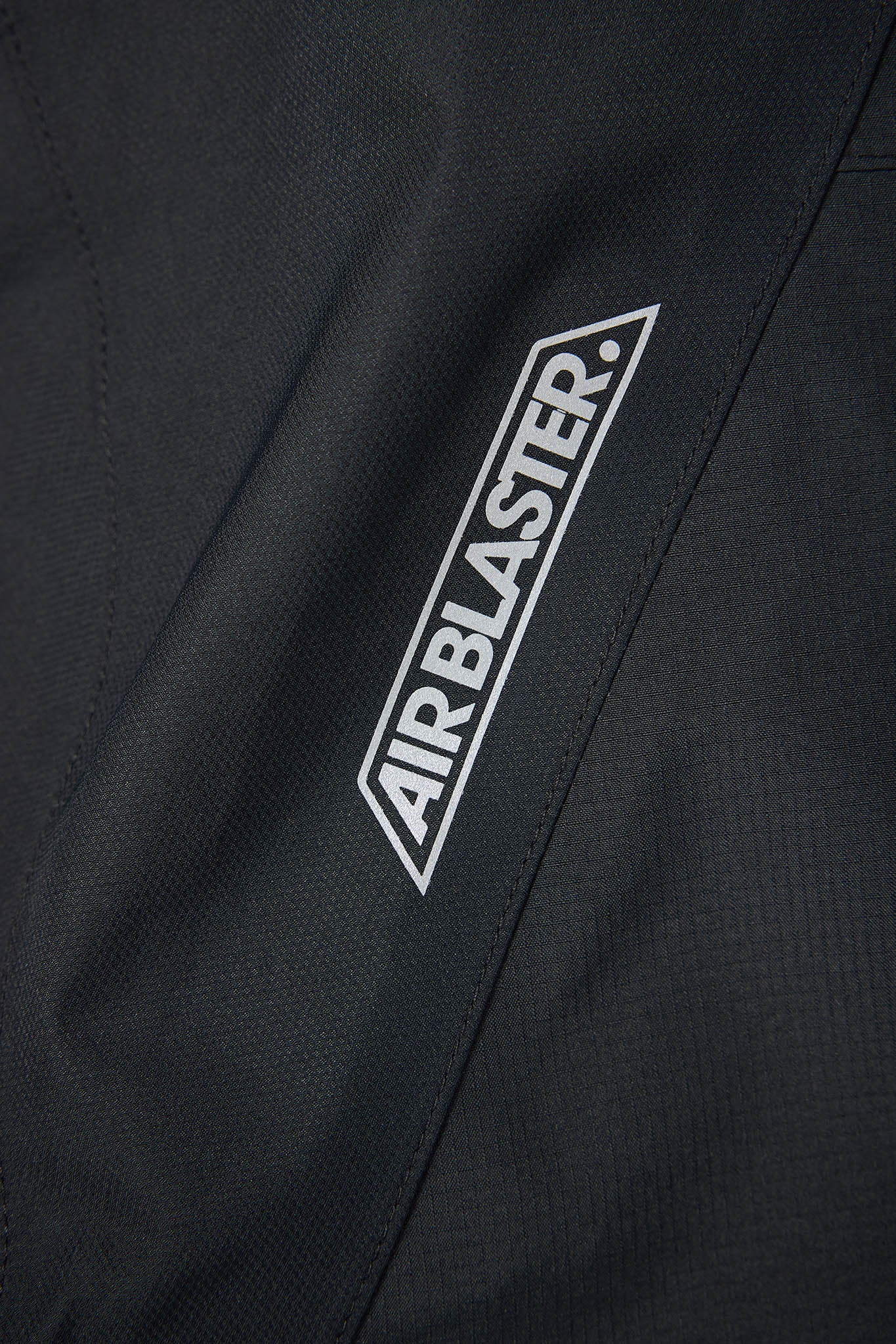 Close-up of a black jacket with 'AIRBLASTER' logo on a dark background