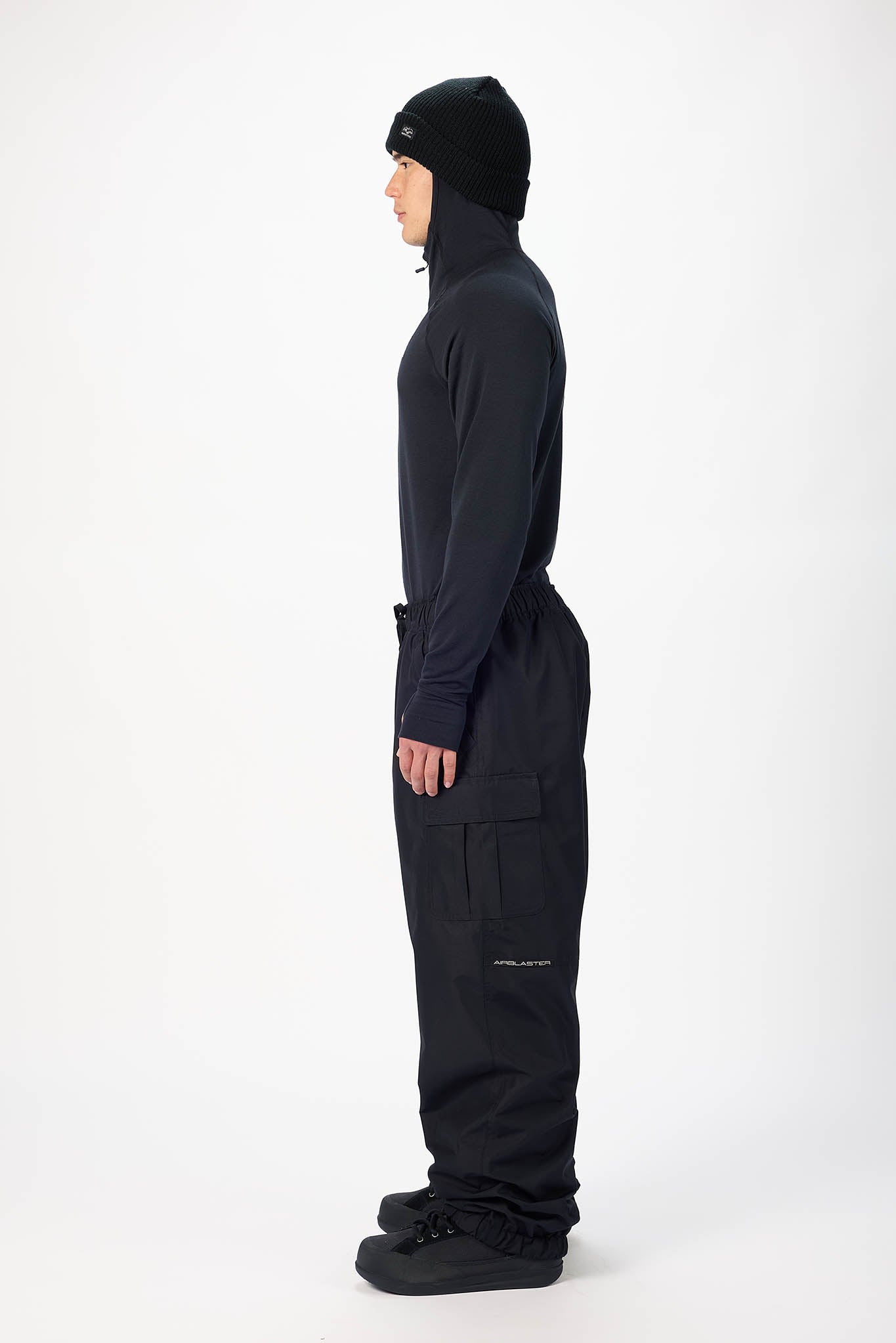 A model shown in profile wearing a black hooded jacket, black cargo pants, and black boots against a plain white studio background.