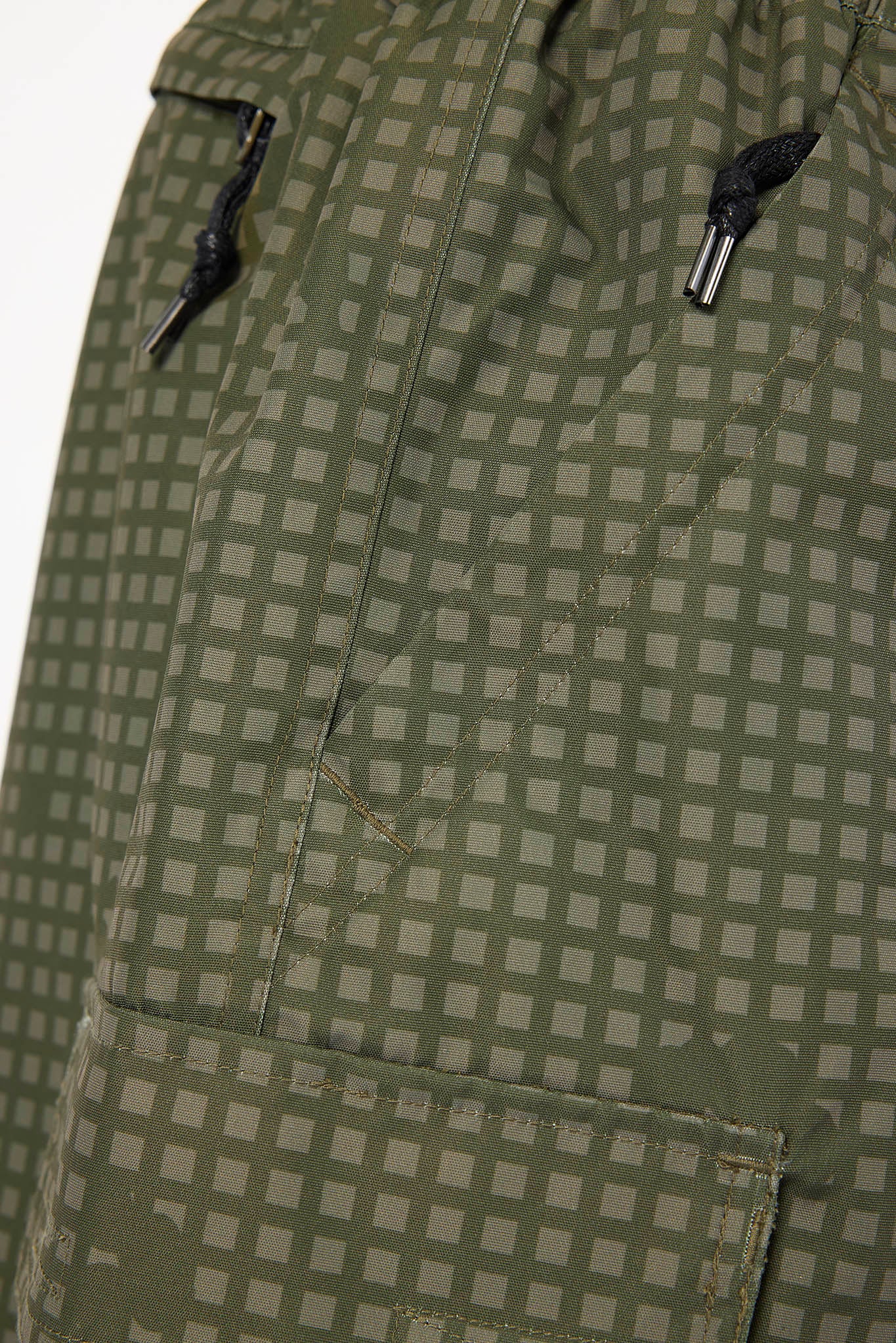 Close-up of olive green and gray checkered fabric with black drawcords on a zipper pocket.