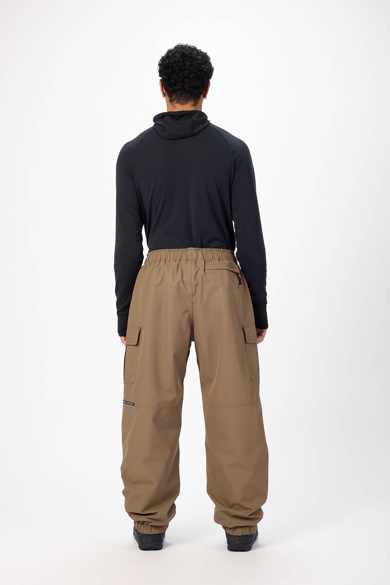 A model shown from the back wearing a black long-sleeve mock-neck top and wide-leg brown cargo pants against a plain white studio background.