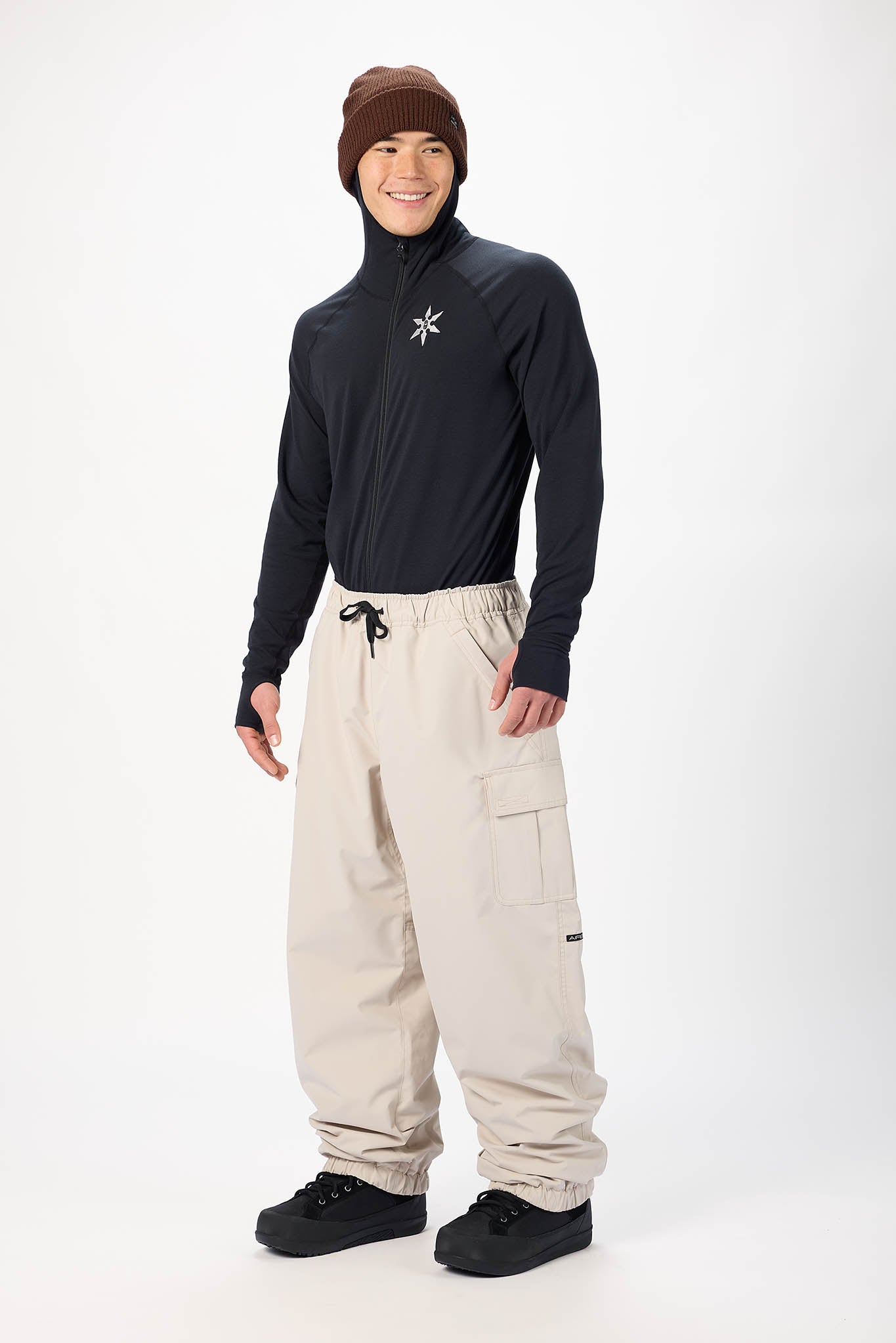 A man modeling a black long-sleeve quarter-zip turtleneck and beige snow pants against a plain white studio background.