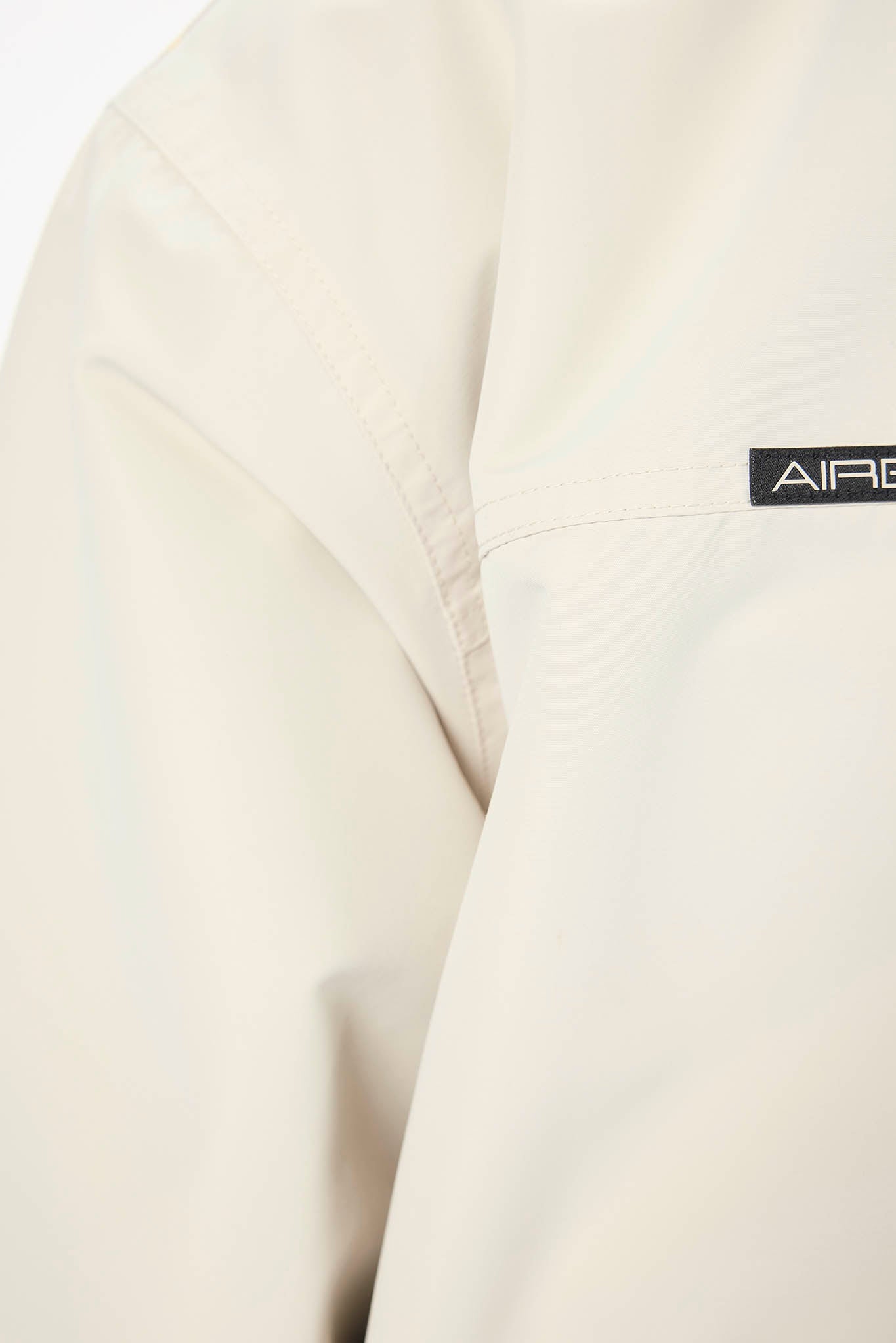 Close-up of a light cream-colored jacket sleeve with a black rectangular patch displaying the partial brand name 'AIRB'.