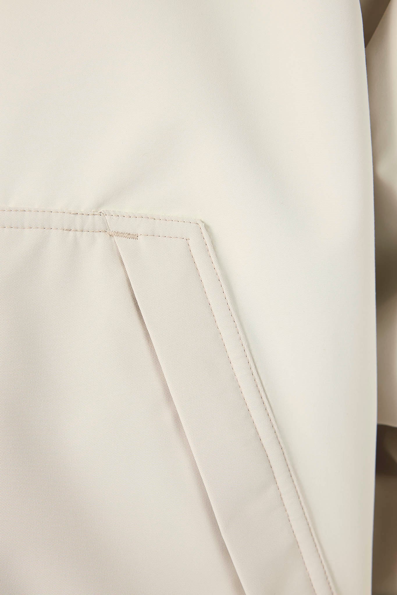 Close-up detail of a light cream or off-white fabric garment, showing a folded corner with fine stitching.
