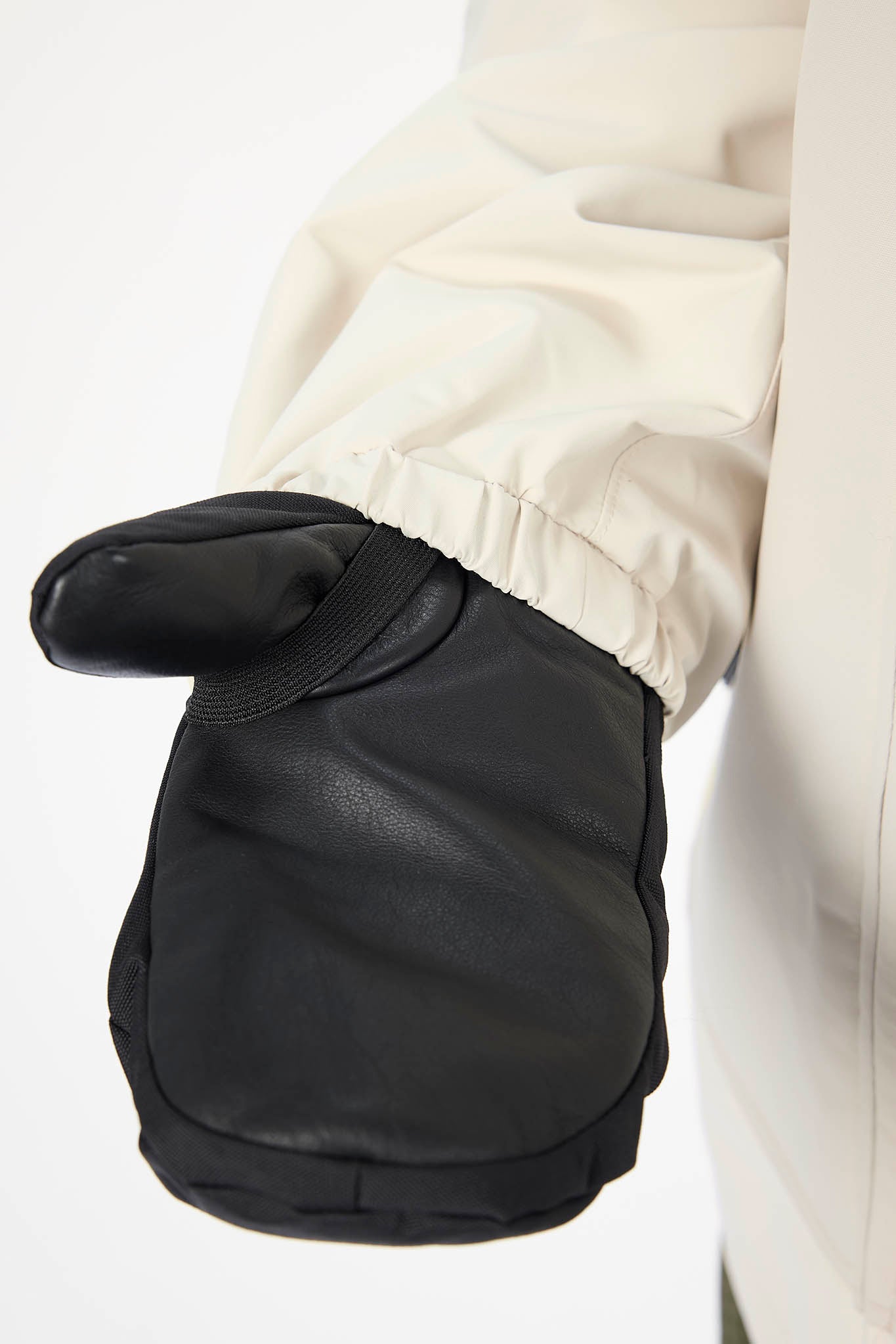 A close-up of a black leather mitten with a thumb loop, worn on a hand with a cream-colored sleeve visible at the top.