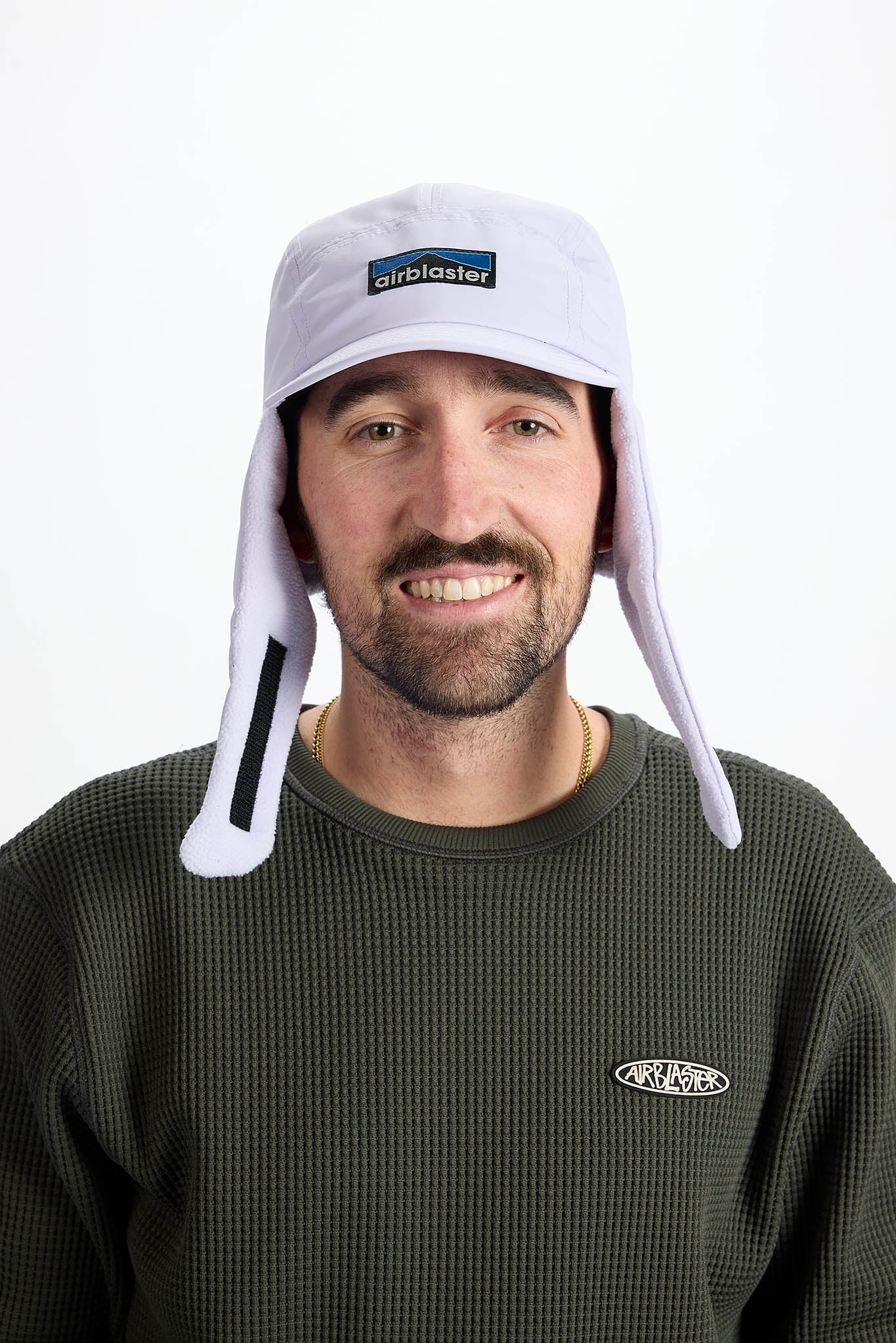 A man wearing a white wintery sun hat with ear flaps and a chin strap, on white background.
