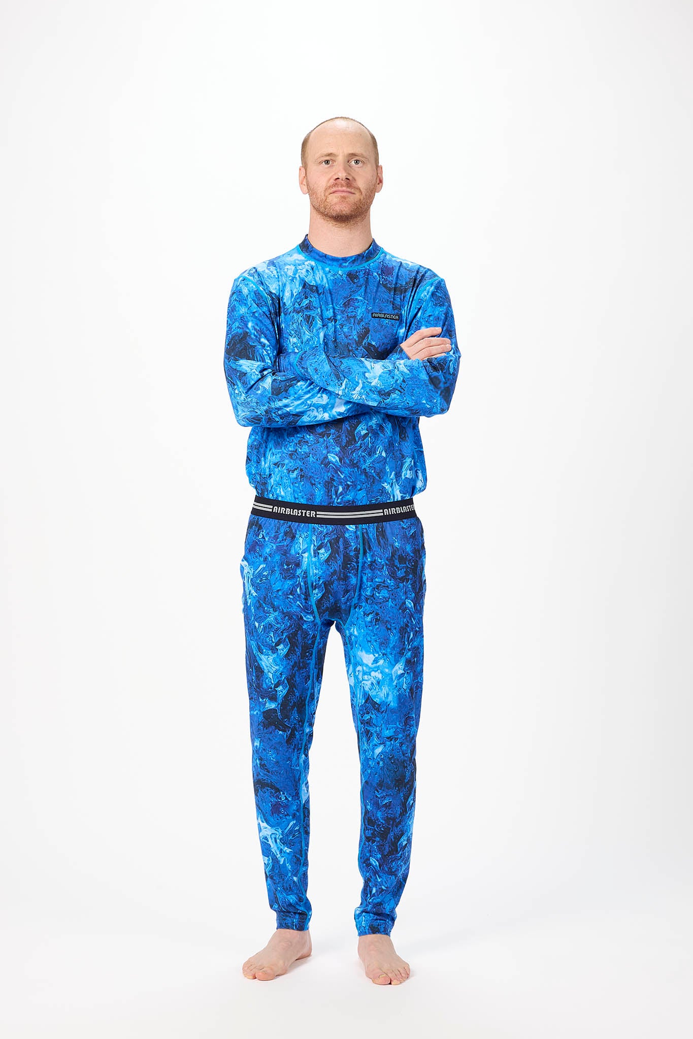 A man wearing a blue and black abstract patterned long-sleeve base layer set, standing against a plain white studio background.
