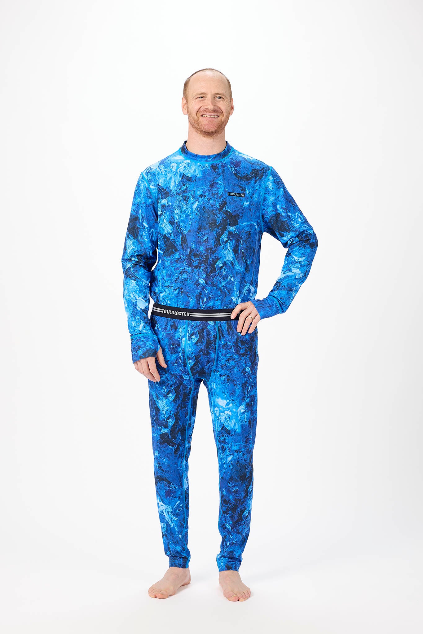 A man wearing a blue and black abstract patterned long-sleeve base layer set, standing against a plain white studio background.