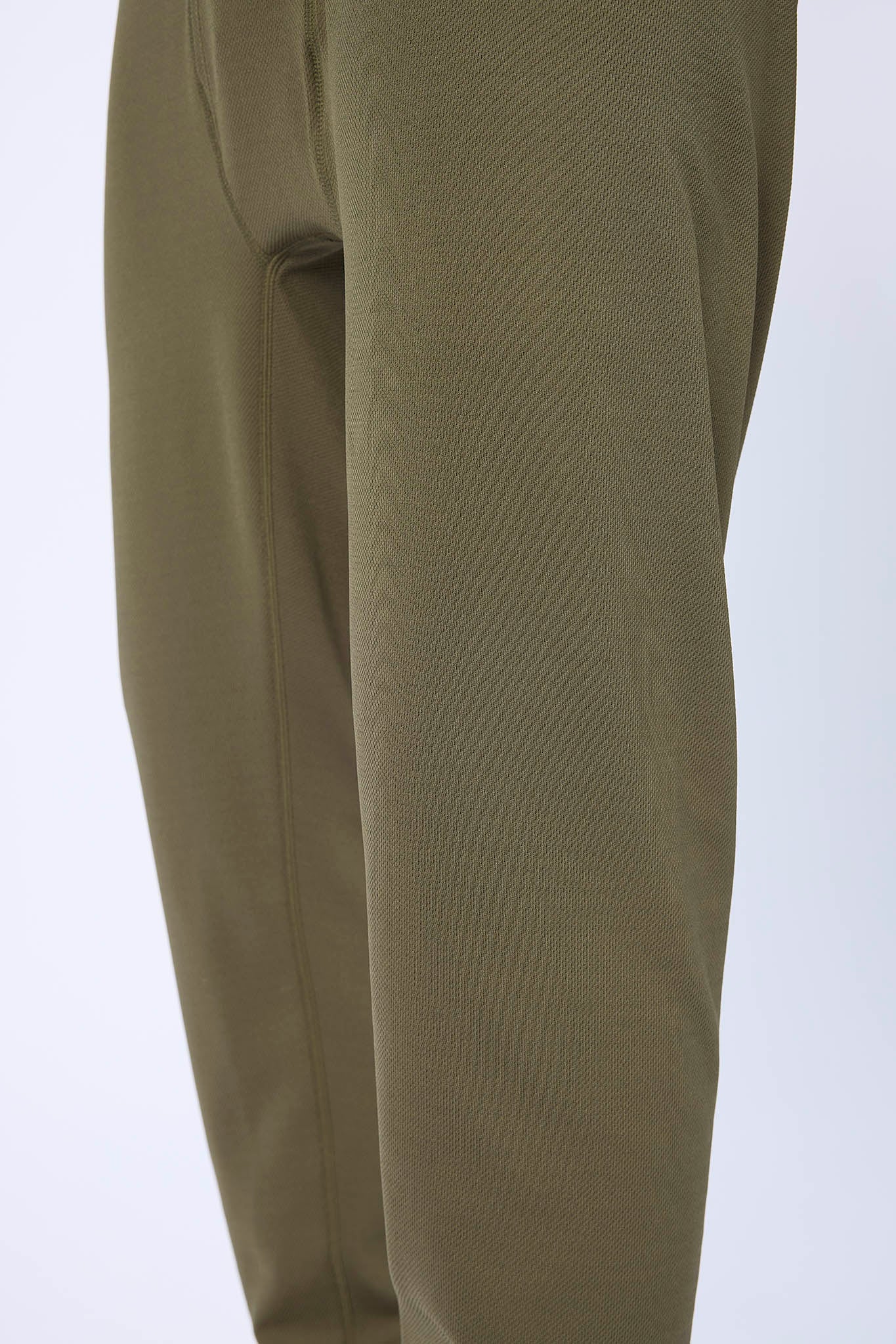 Close-up of olive green pants showing the fabric texture and side seam detail against a plain light background.