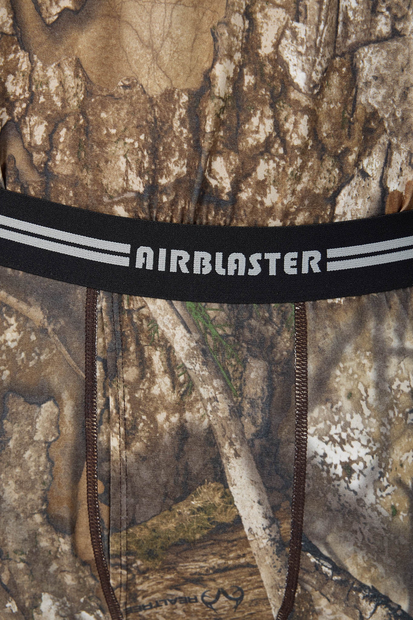 Close-up of a camouflage-patterned garment with a black waistband featuring the AIRBLASTER brand name in white text, with two brown drawstrings hanging down.