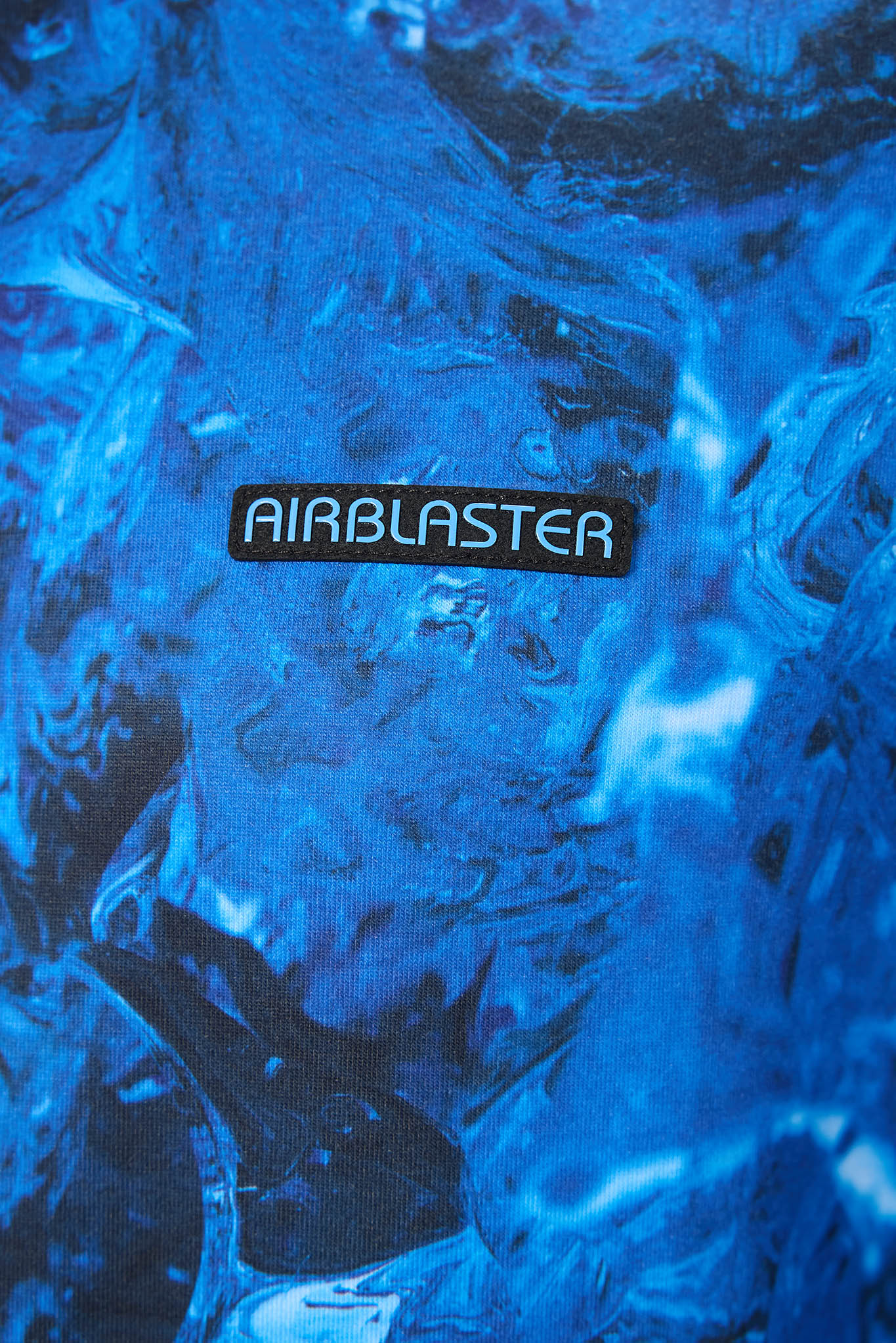 A close-up of a blue textured surface with an embossed or printed AIRBLASTER logo patch in the center.