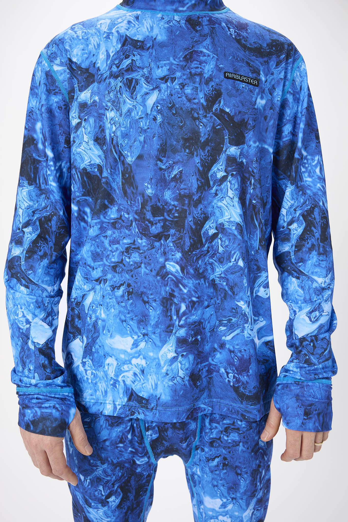 A person shown from the back wearing a blue long-sleeve top and matching blue pants with an abstract marbled pattern. A small black brand patch reading 'AIR BLASTER'