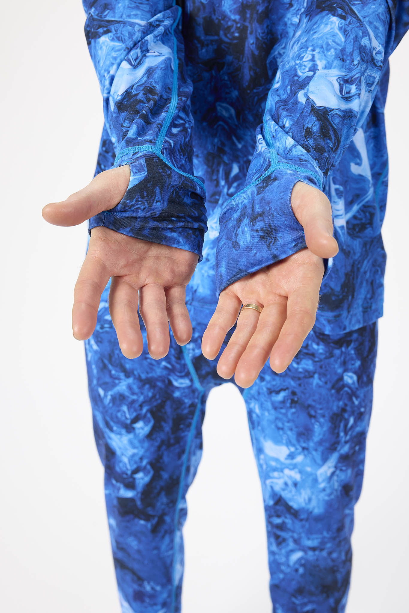 A close-up of a person wearing a blue long-sleeve camouflage-patterned top and matching blue pants, with both hands shown against a plain light background.