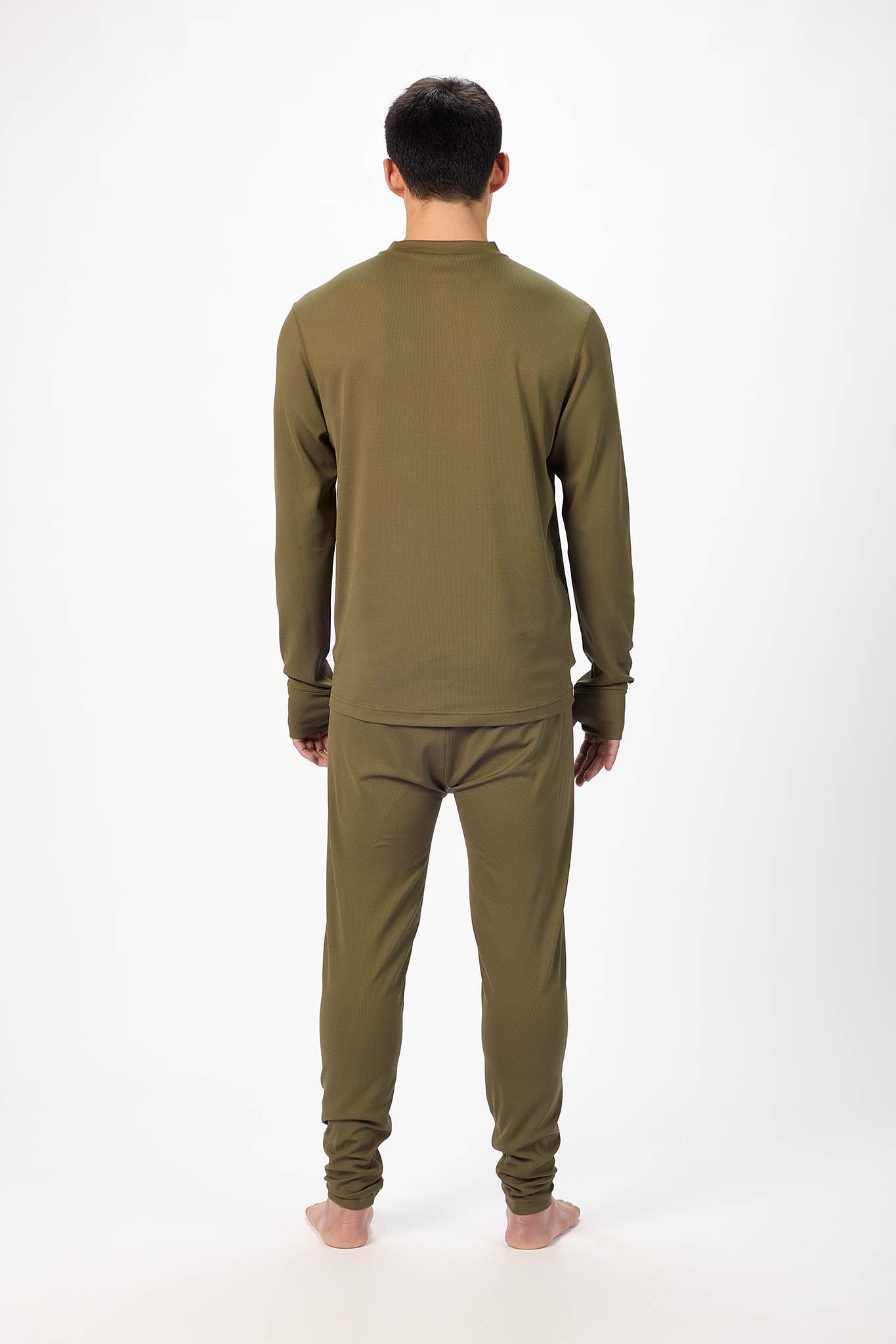 A man viewed from the back wearing an olive green long-sleeve top and matching pants, standing against a plain white studio background.