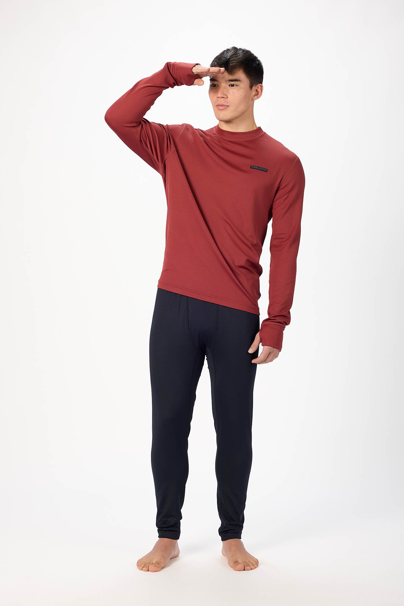 A man modeling a long-sleeve crewneck shirt in a deep red color, paired with dark navy pants, standing against a plain white studio background.