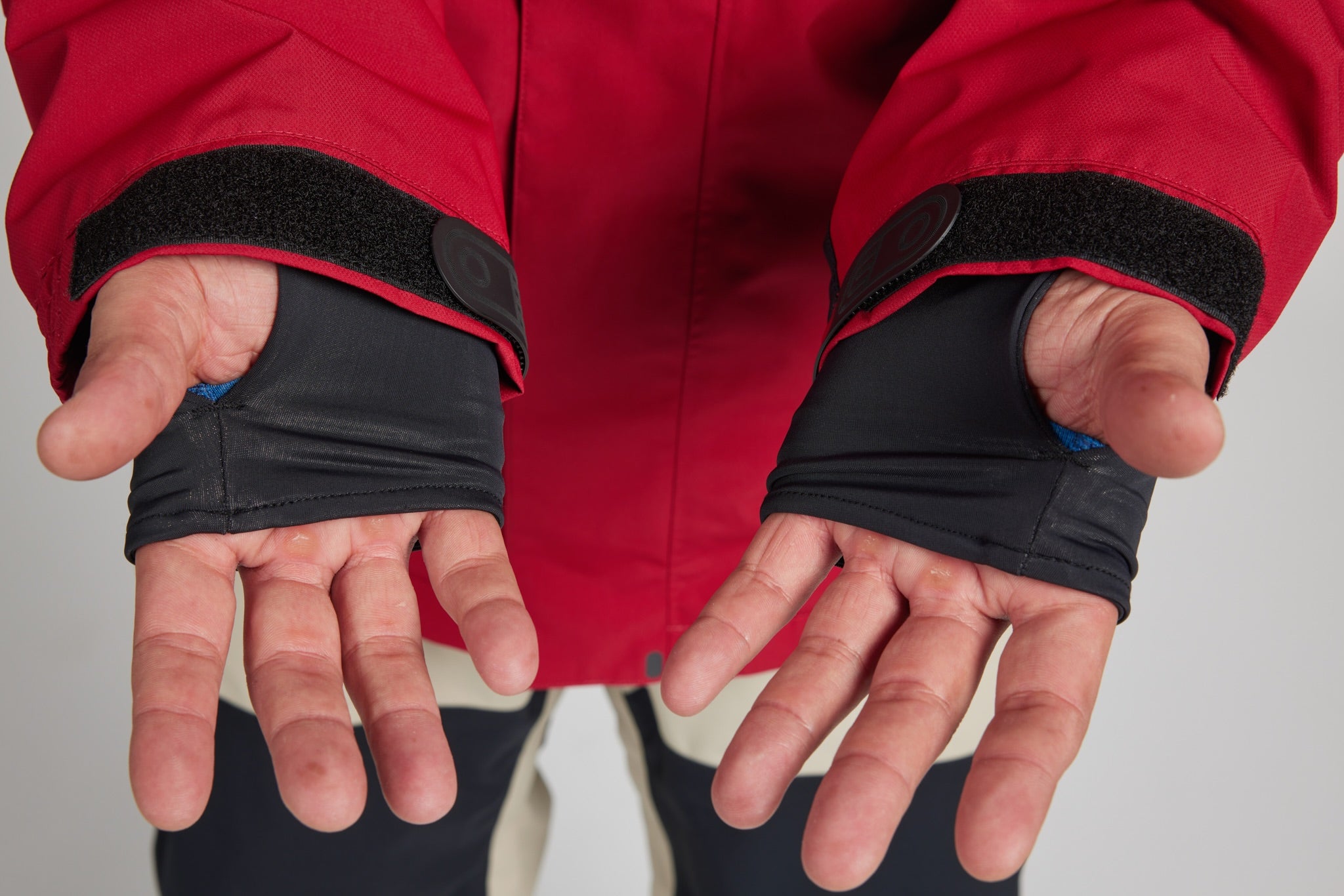 Close-up of a person wearing black fingerless glove sleeves under a red jacket, with both hands shown against a light gray background.