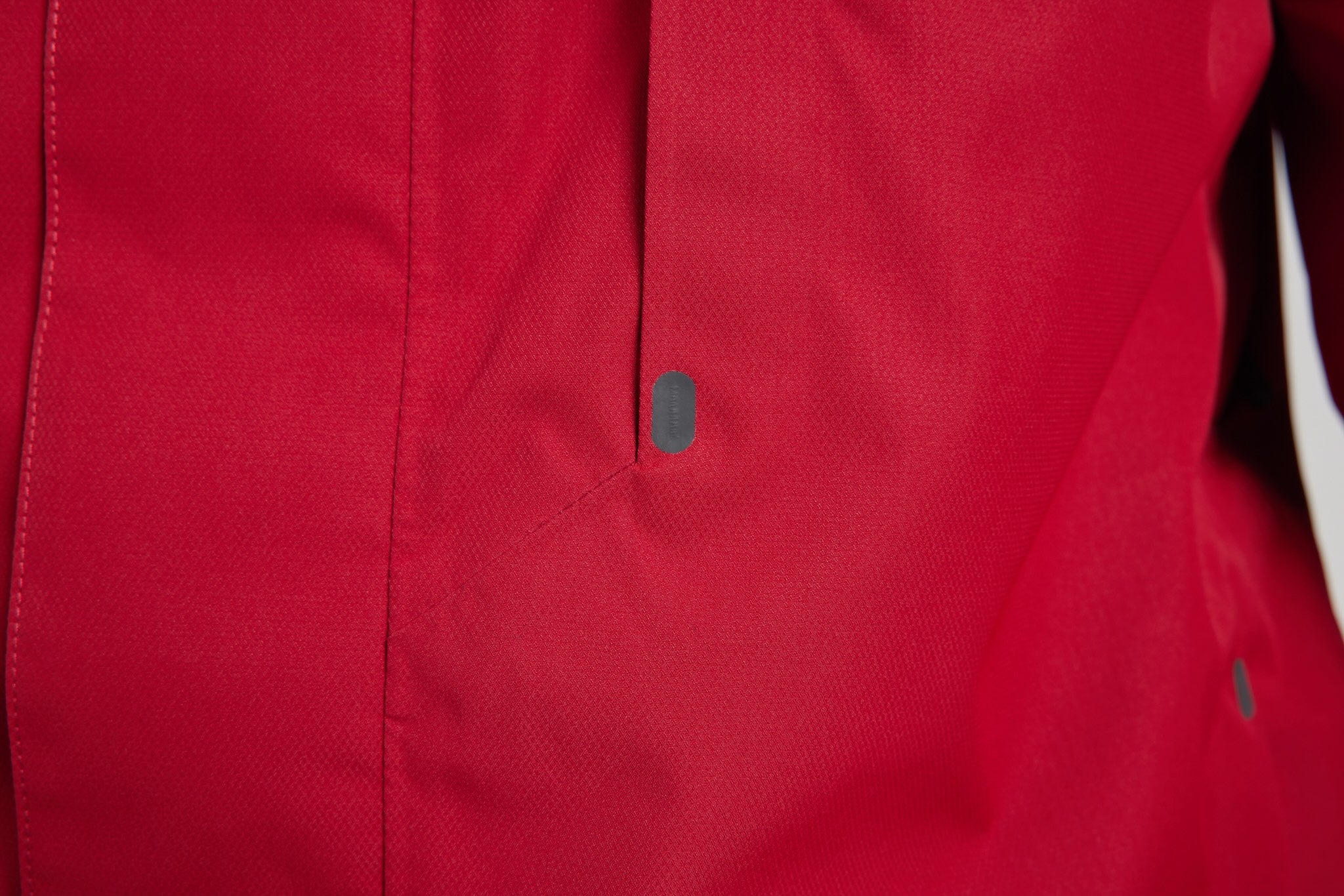 Close-up of a red textured fabric garment with a vertical seam and a small dark oval detail near the center.