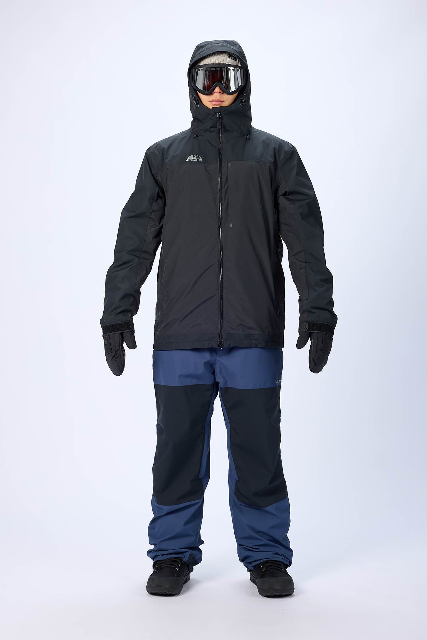 Person wearing a black and blue snowsuit with goggles on a white background
