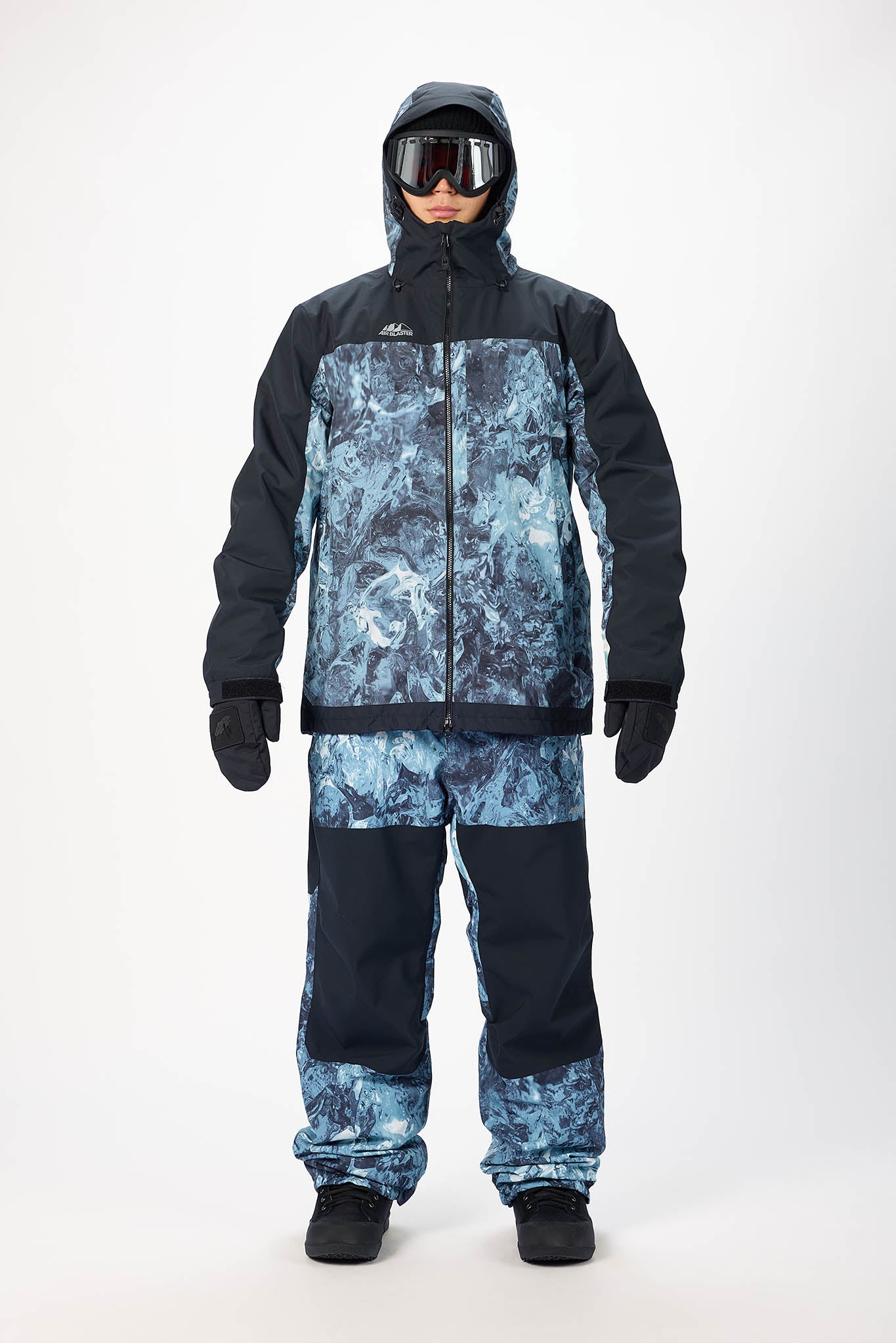 Person wearing a black and blue camouflage snowsuit with goggles on a white background