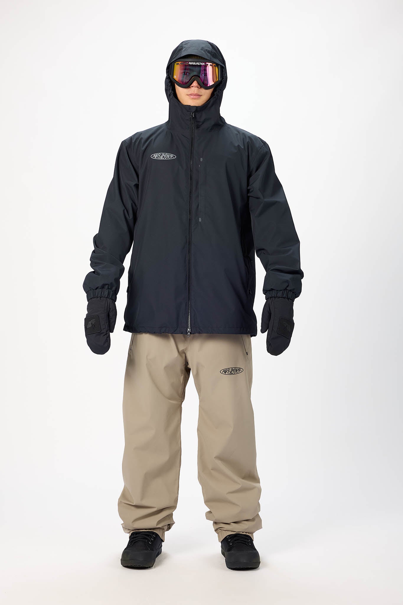 Person wearing a black jacket and beige pants with goggles on a white background
