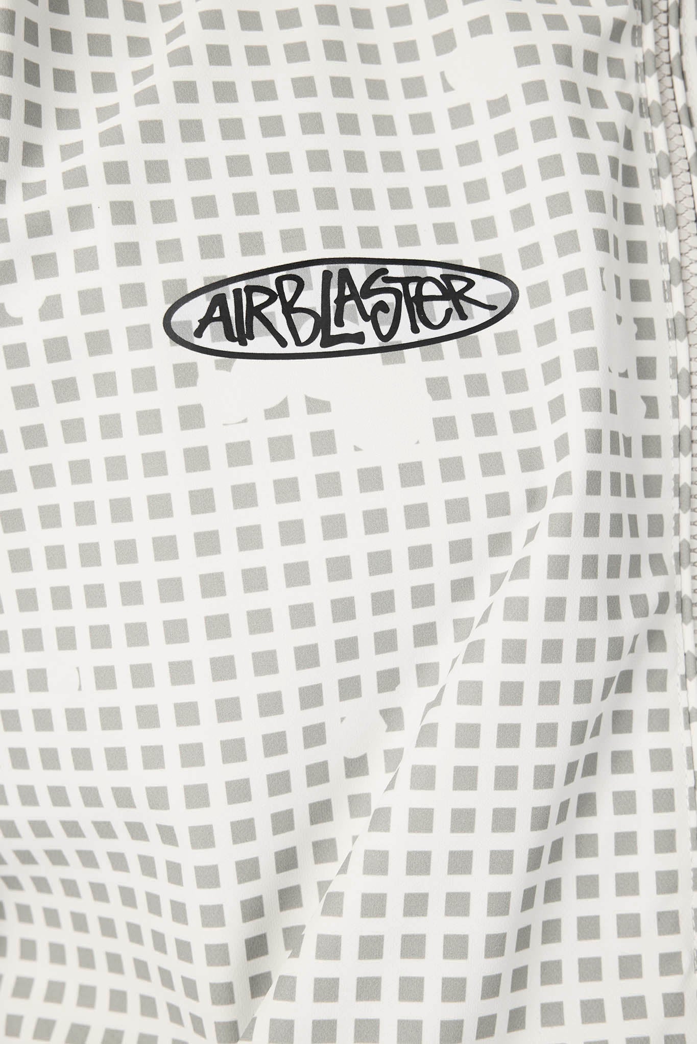 Close-up of a white fabric with a light gray grid pattern and a black oval Airblaster logo patch.