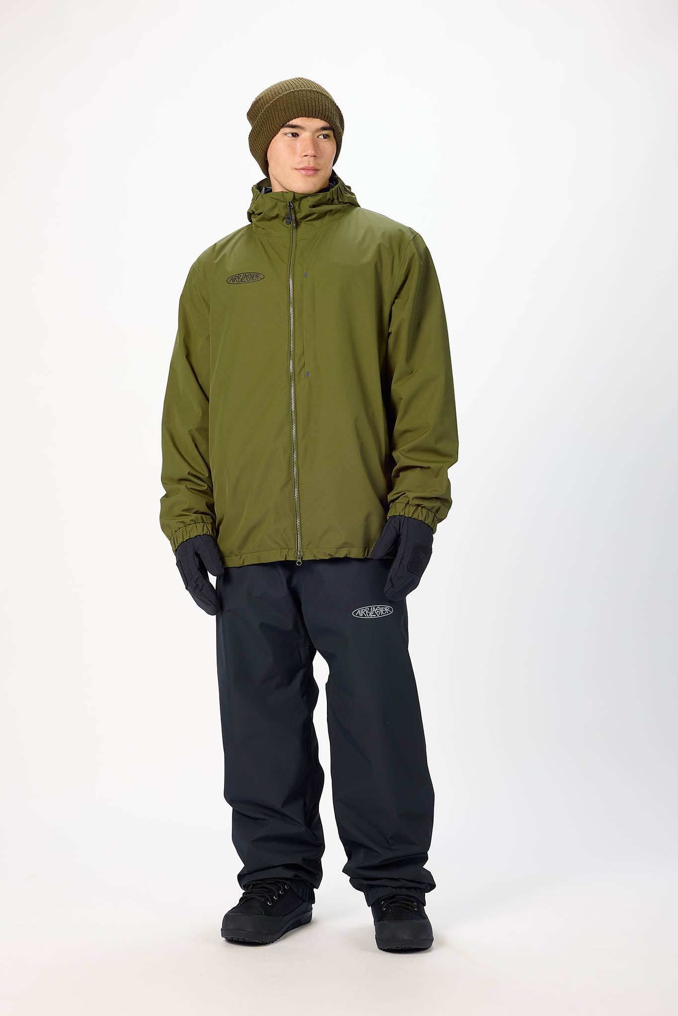 Person wearing an olive green jacket and black pants on a white background