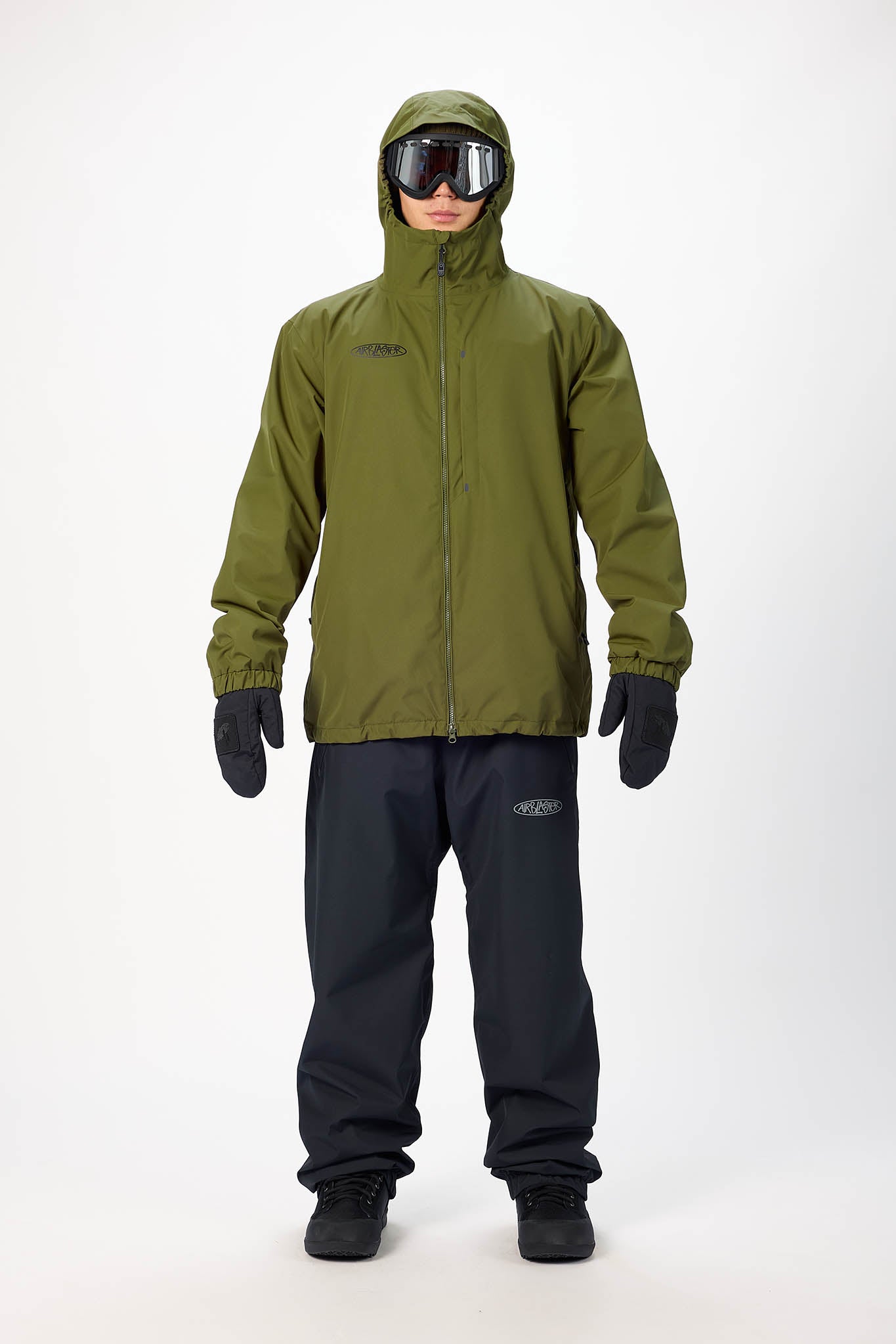 Person wearing a green jacket and black pants with goggles on a white background