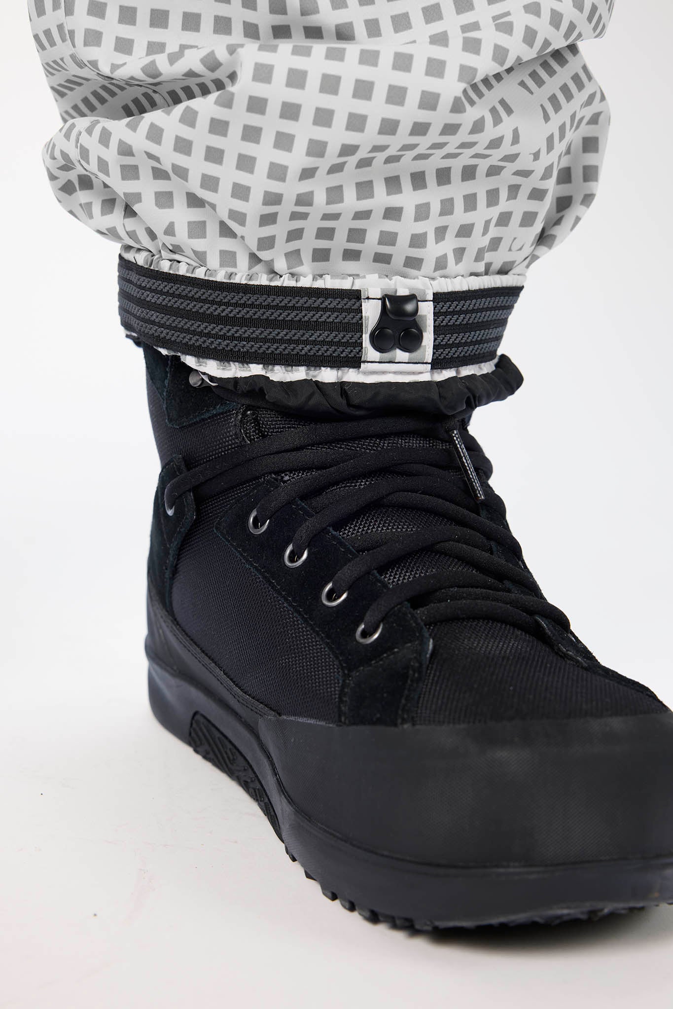 Black winter boot with a checkered pants cuff on a white background
