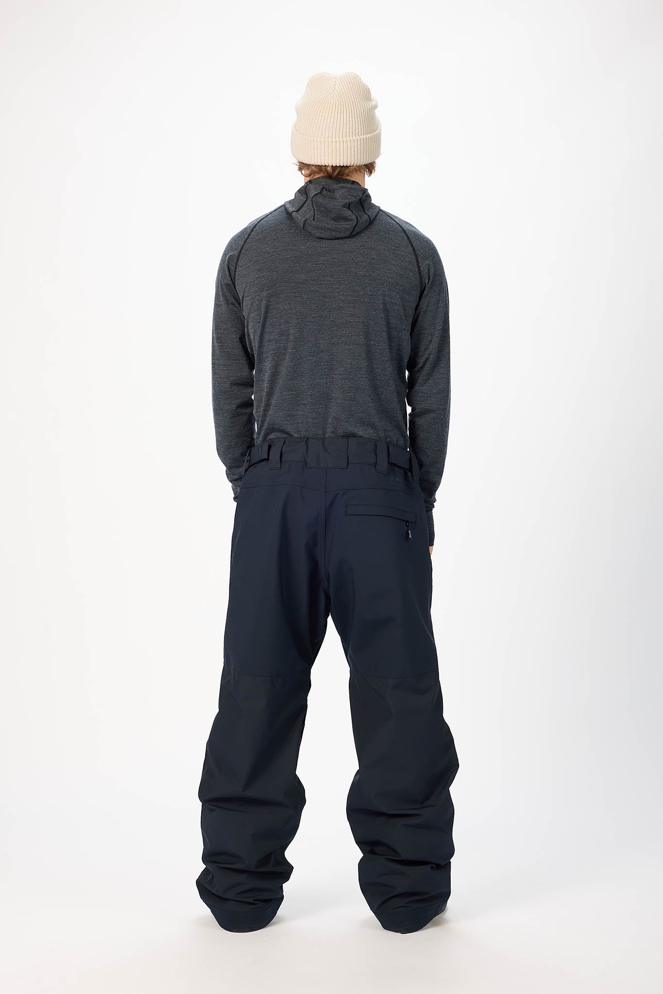 Person wearing a dark gray snowsuit and beige beanie on a white background