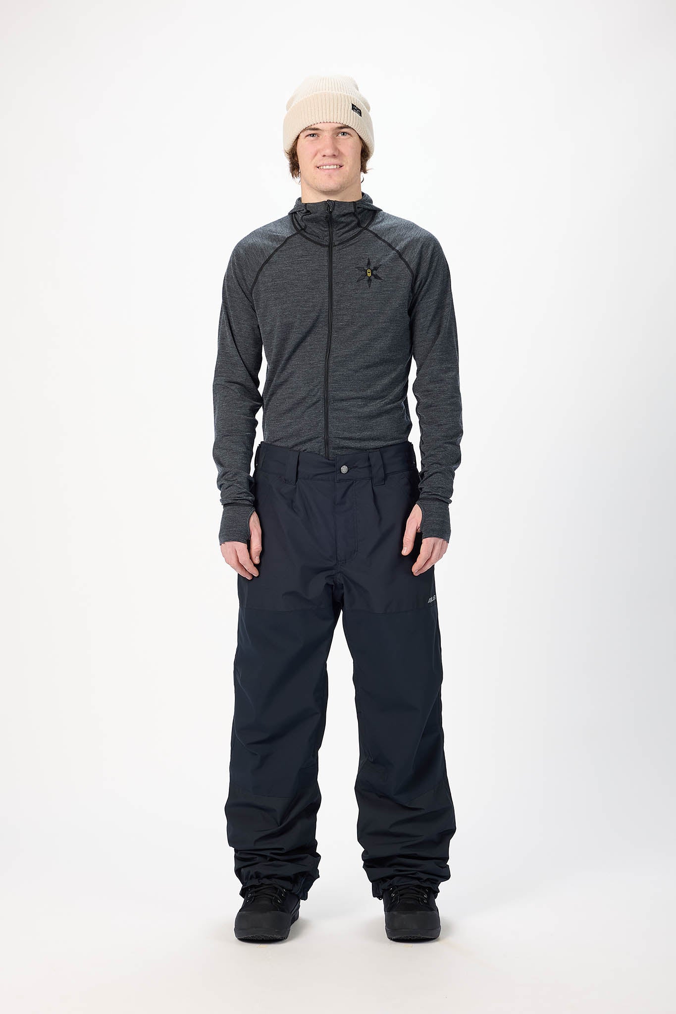 Person wearing a gray jacket and black snow pants on a white background