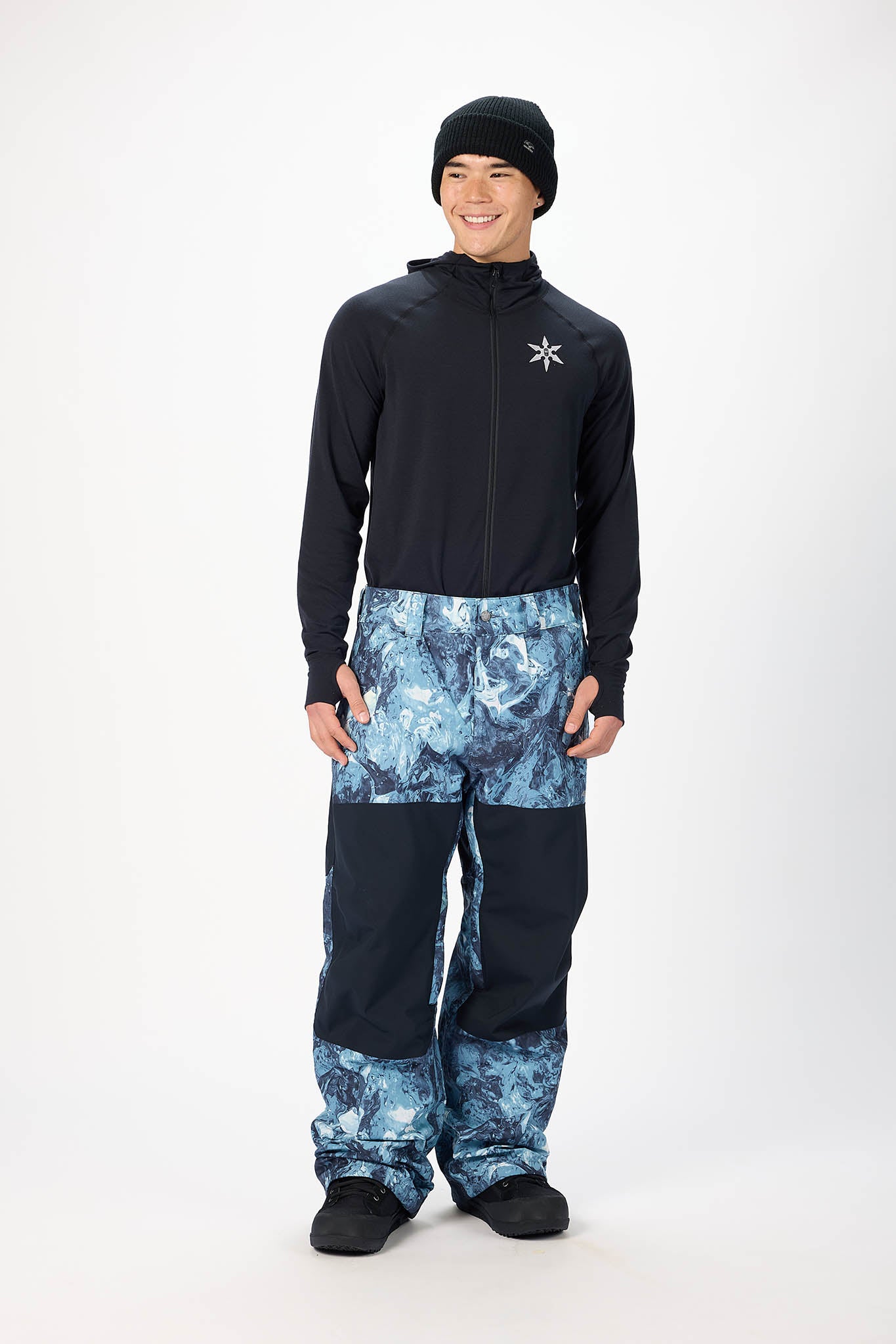 Person wearing a black jacket and blue patterned pants on a white background