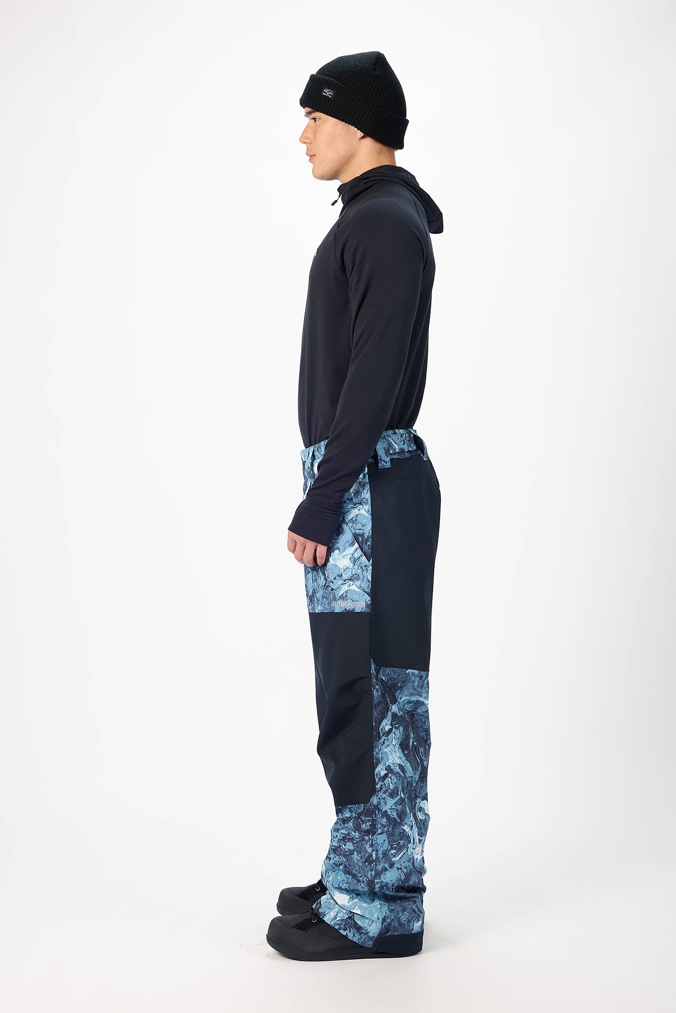Person wearing a black jacket and blue patterned pants on a white background
