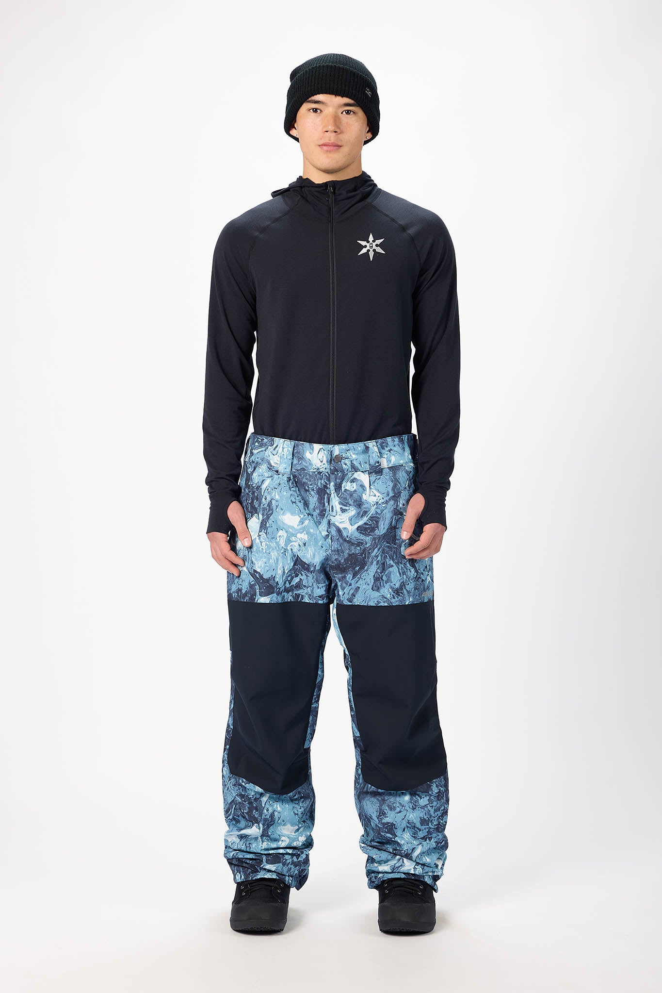 Person wearing a black jacket and blue camouflage pants on a white background