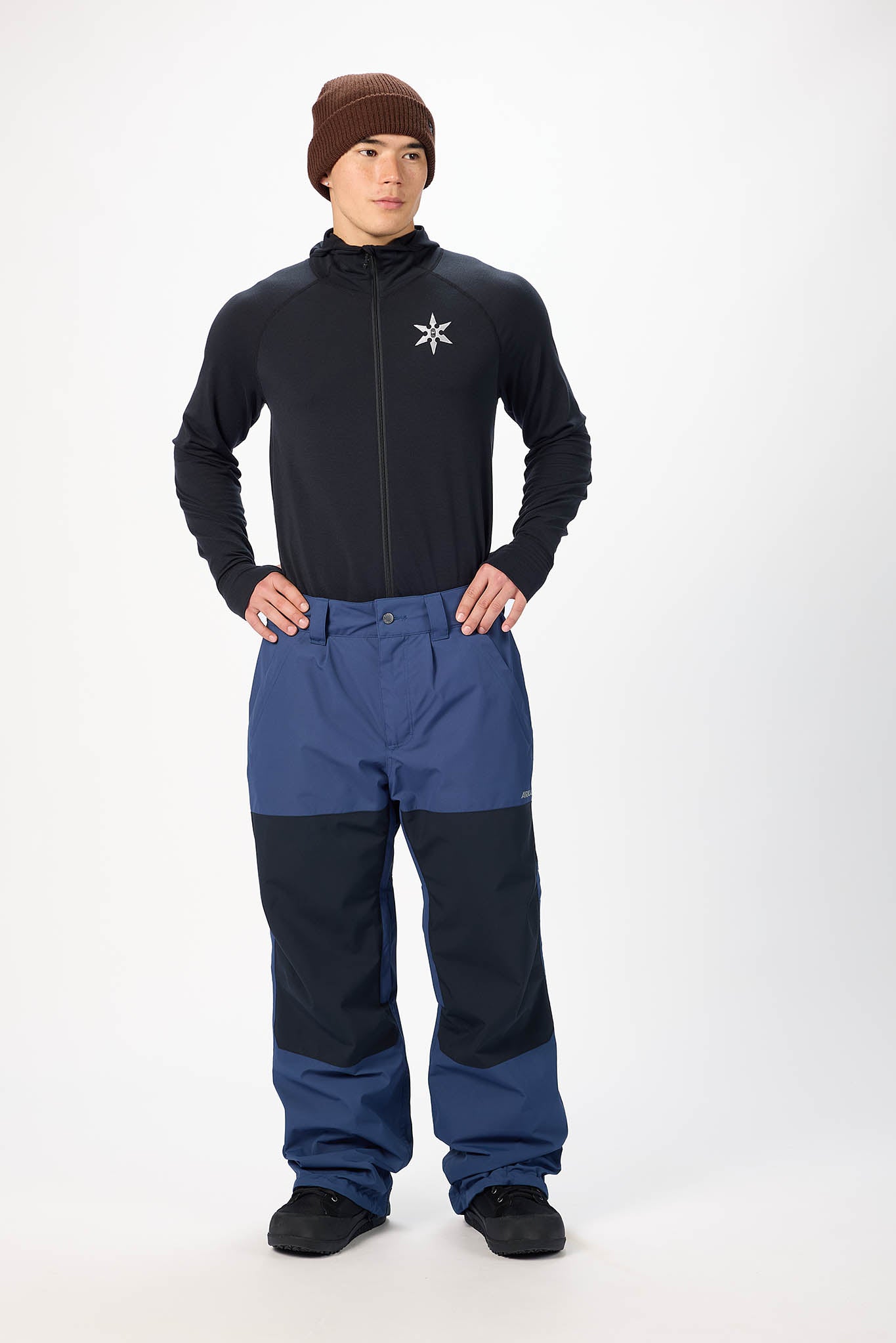 Person wearing a black jacket with a white logo and blue pants on a white background
