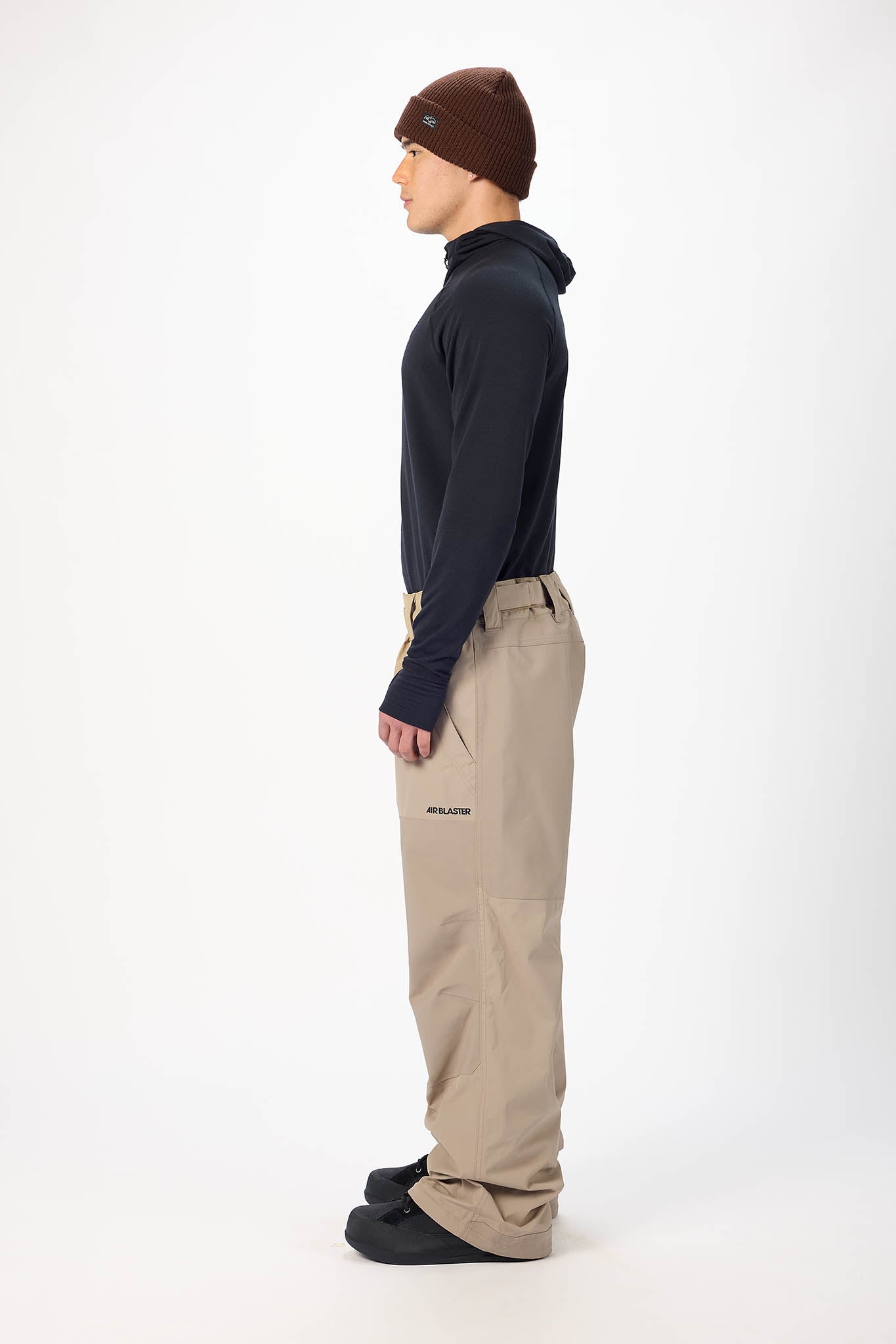 Person wearing a dark long-sleeve shirt, brown beanie, and beige pants on a white background