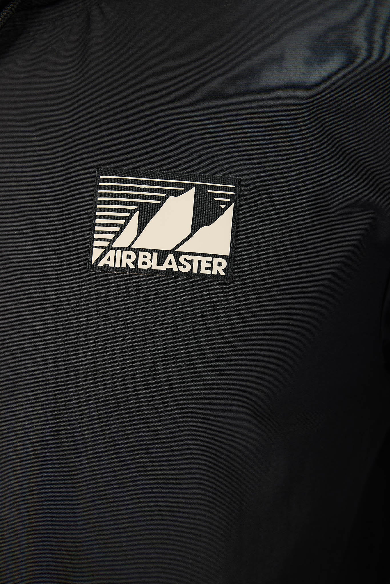 Close-up of a black jacket or windbreaker with a rectangular Air Blaster logo patch on the chest.