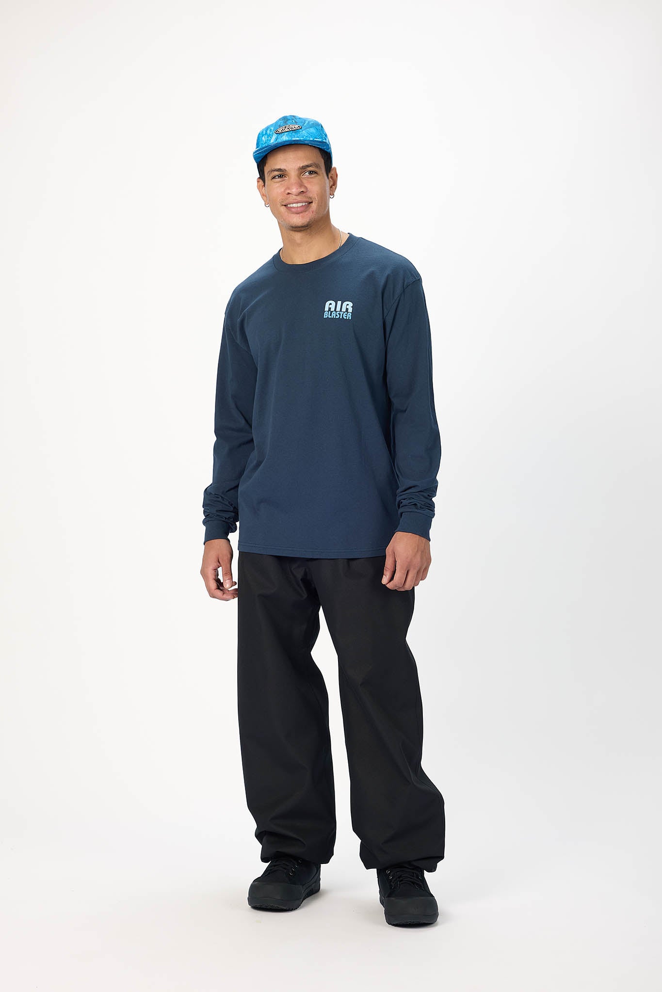 A man modeling a dark navy blue long-sleeve t-shirt with a small white 'AIR' logo on the left chest, paired with black pants and a blue cap, standing against a plain white studio background.