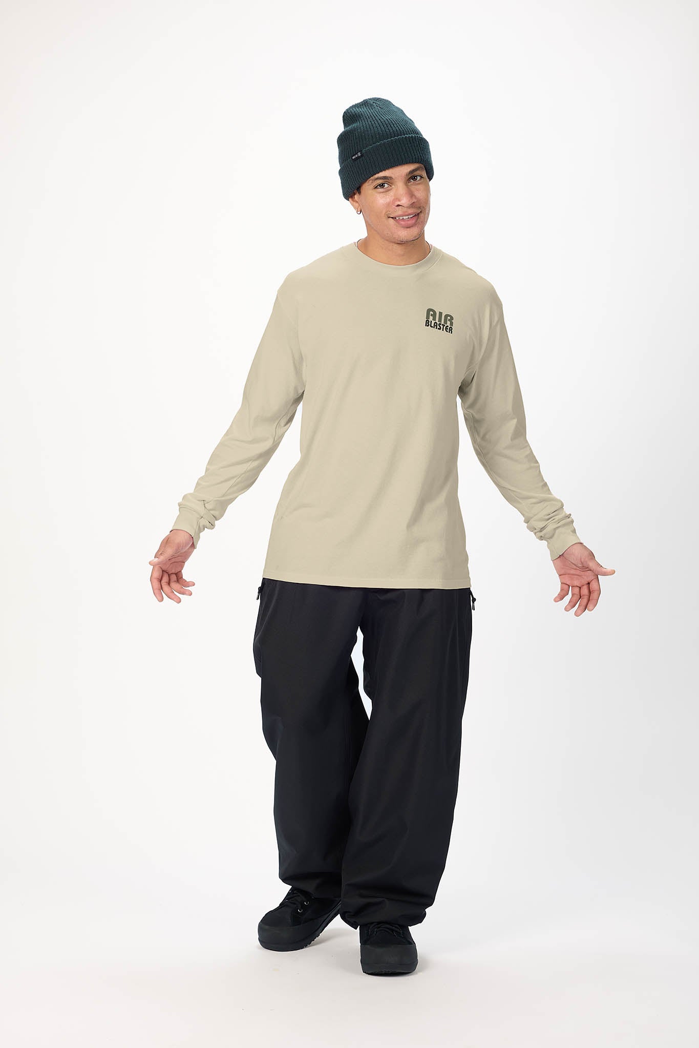 A model wearing a beige long-sleeve crewneck shirt with a black 'PLAT' logo on the left chest, black baggy pants, black shoes, and a dark green beanie, standing against a white studio background.