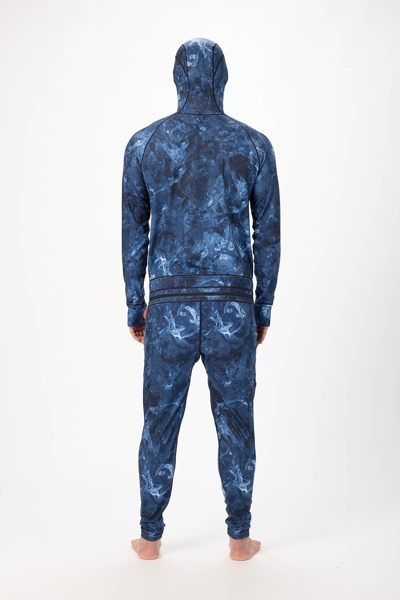 behind view A man wearing a blue swirl patterned onesie with a hooded with a zipper and jogger pants, standing against a plain white studio background.