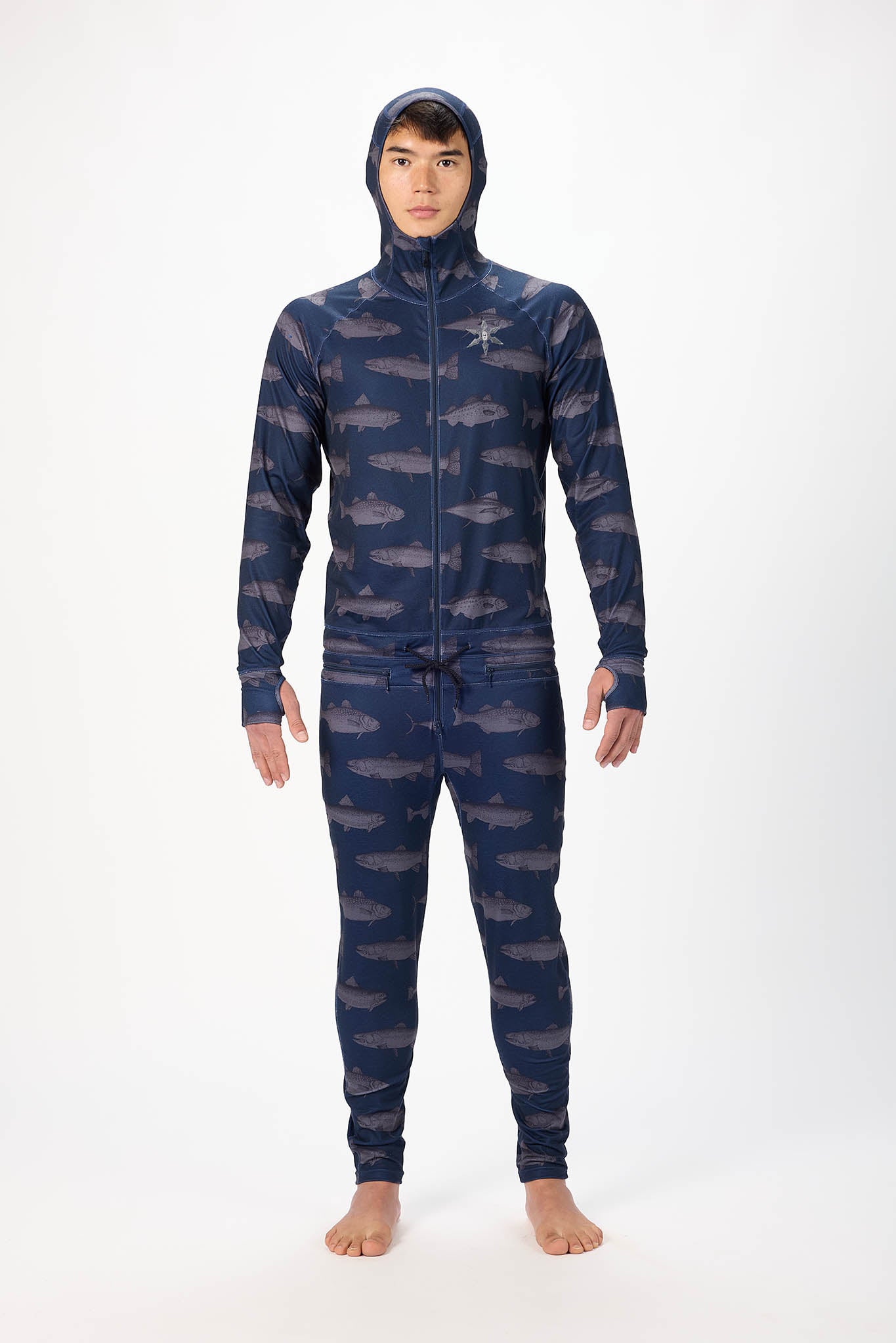 A man wearing a fish patterned onesie with a hooded with a zipper and jogger pants, standing against a plain white studio background.
