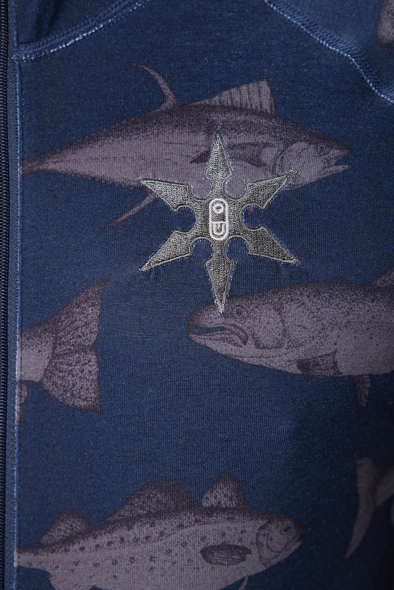 Close-up of a navy blue garment featuring a fish print and a metallic silver star-shaped patch with a central 'PU' emblem.