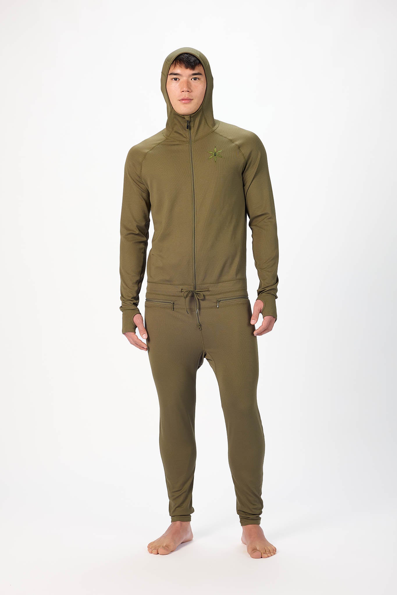 A man wearing a olive onesie with a hooded zip-up jacket and jogger pants, standing against a plain white studio background.