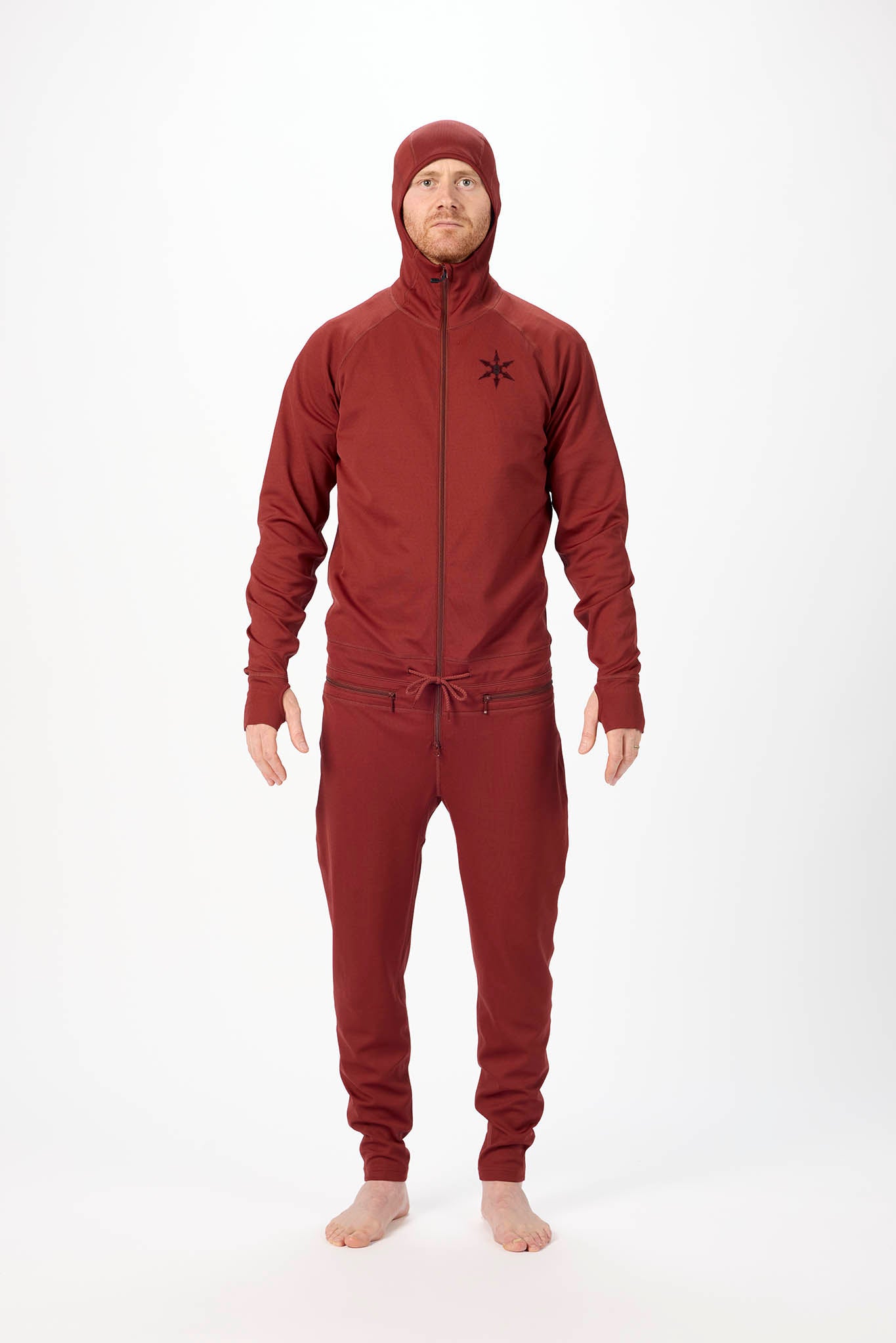 A man wearing a matching burgundy onesie with a hooded zip-up jacket and jogger pants, standing against a plain white studio background.